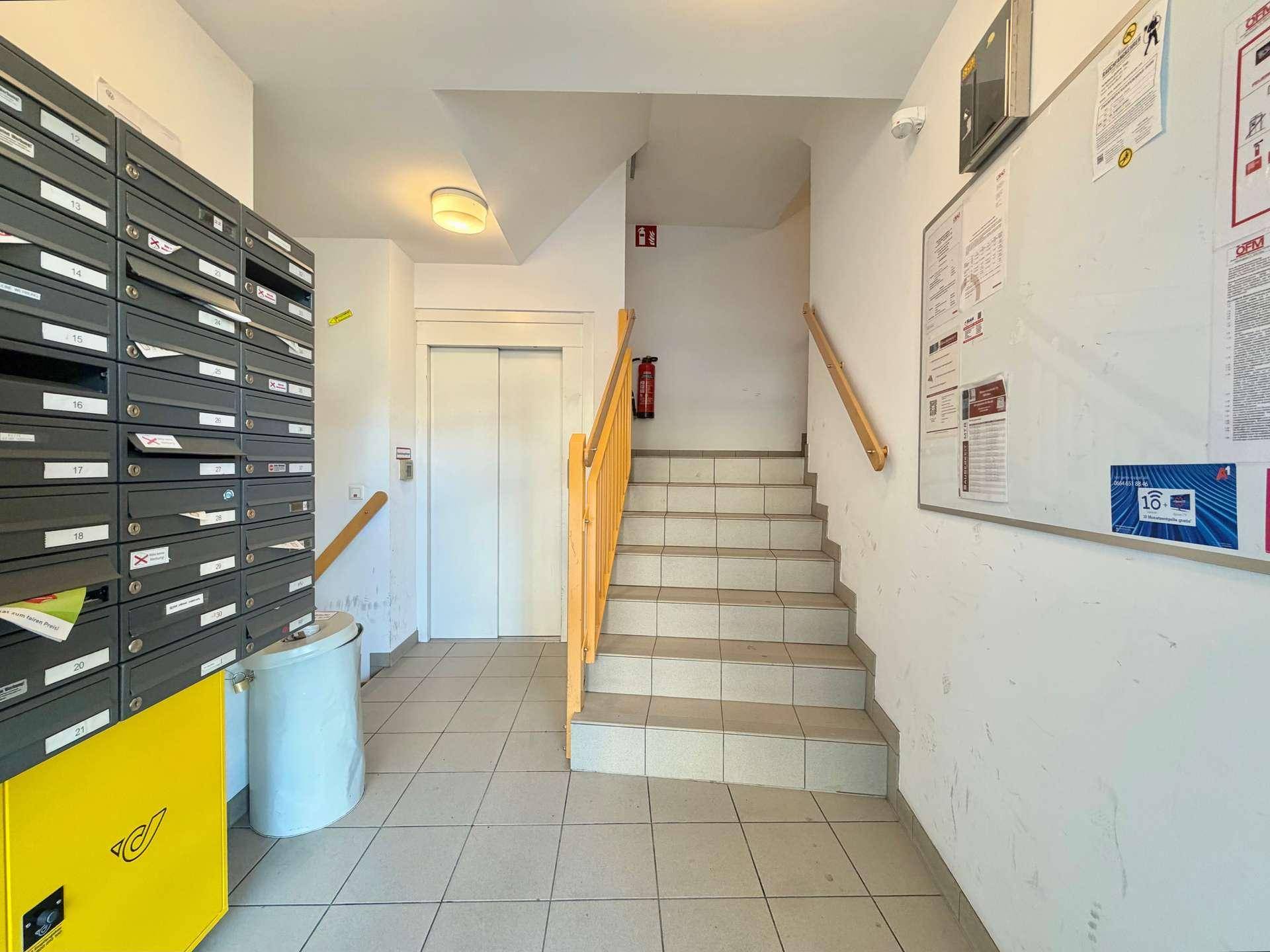 Eingangsbereich mit Briefkästen, Treppenhaus und einem Aufzug, der Zugang zu den Etagen bietet.