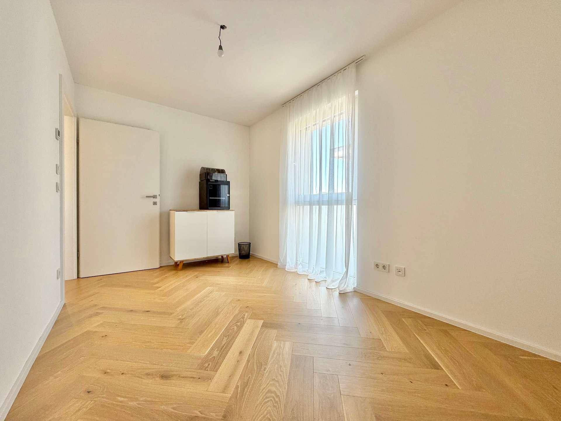 Helles Zimmer mit Fischgrätparkett und großem Fenster, ideal als Gäste- oder Kinderzimmer.