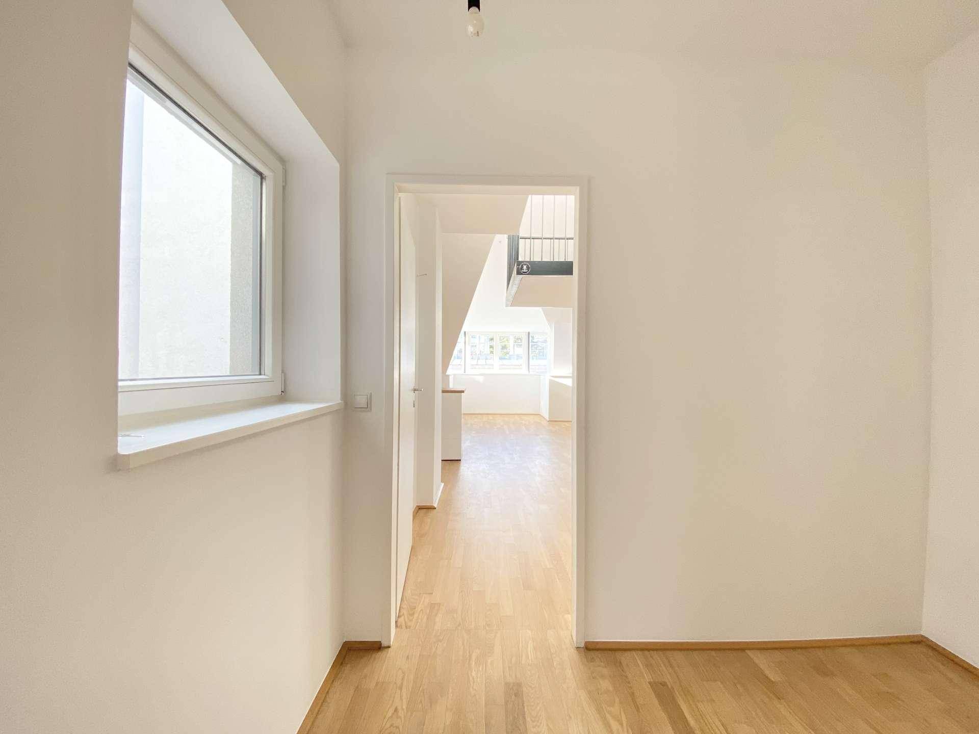 Heller Übergangsbereich mit Holzfußboden und einem Fenster, das Tageslicht hereinlässt.