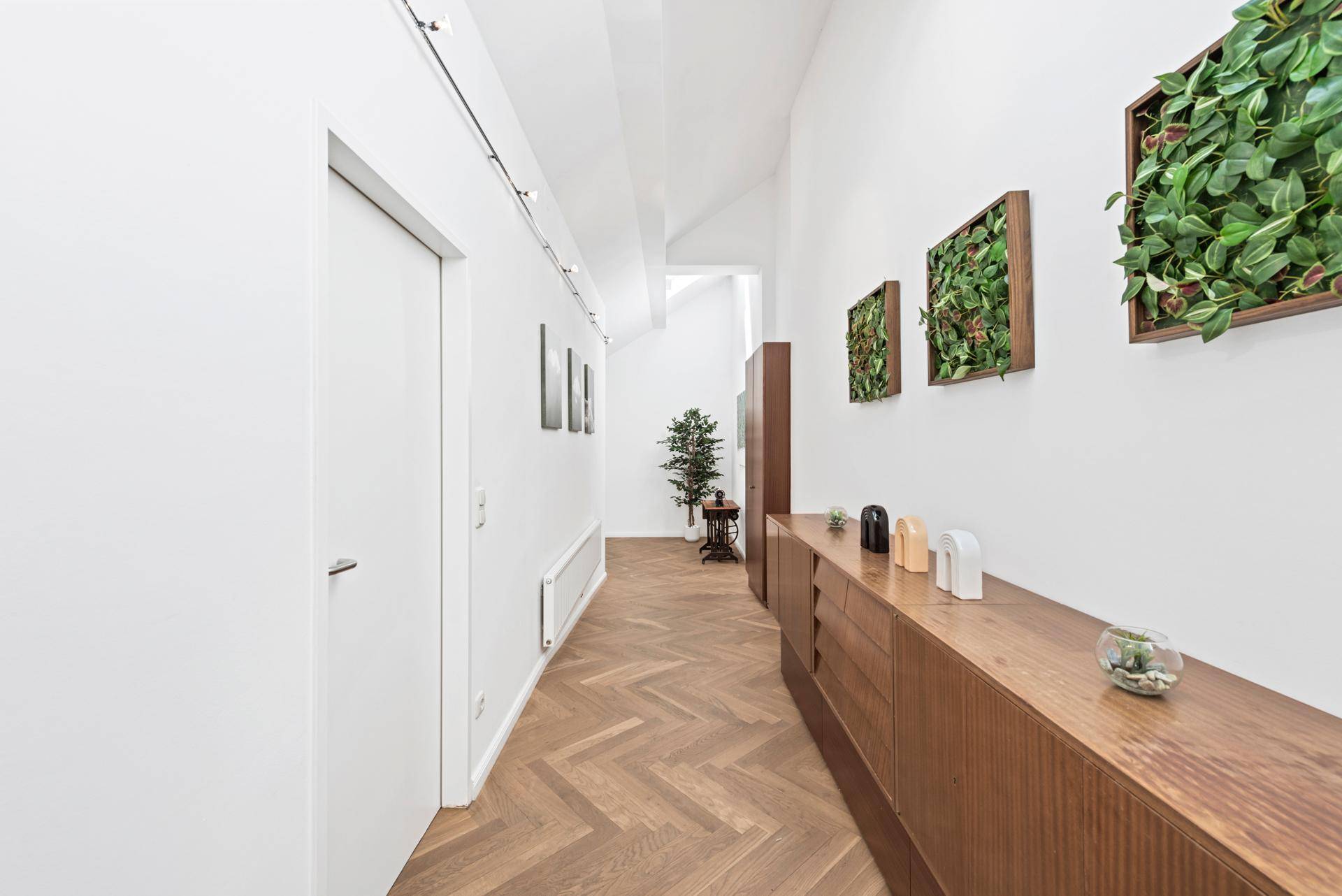 Langer Flur mit Holzsideboard, Fischgrätparkett und grünen Wanddekorationen.