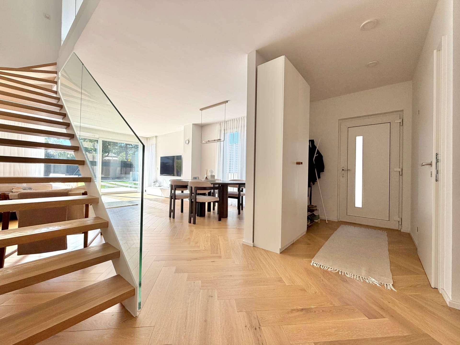 Offener Wohn- und Essbereich mit moderner Holztreppe und Blick auf den Garten.
