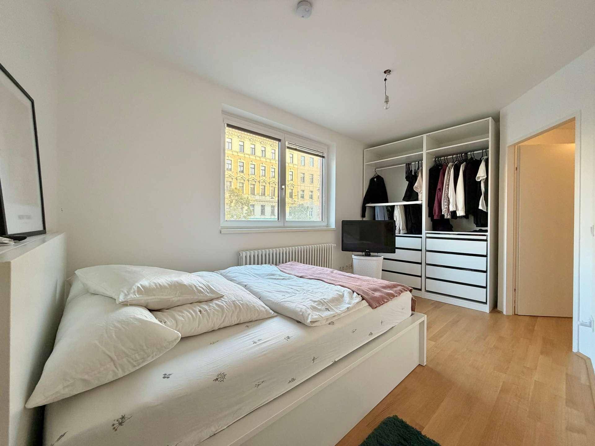 Schlafzimmer mit Doppelbett, offenem Kleiderschrank und Holzfußboden.