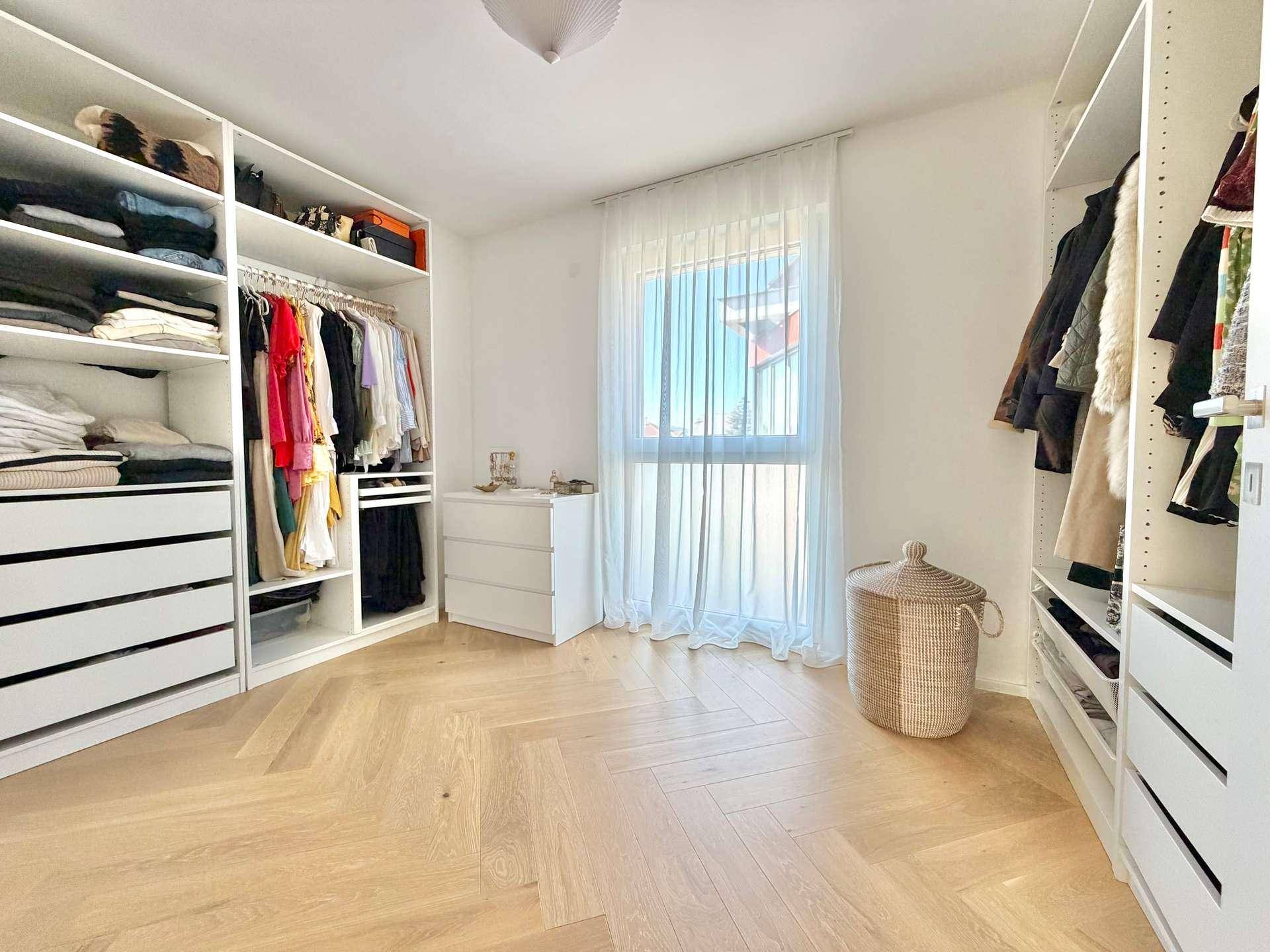 Geräumiger begehbarer Kleiderschrank mit offenen Regalsystemen und Fischgrätparkett.