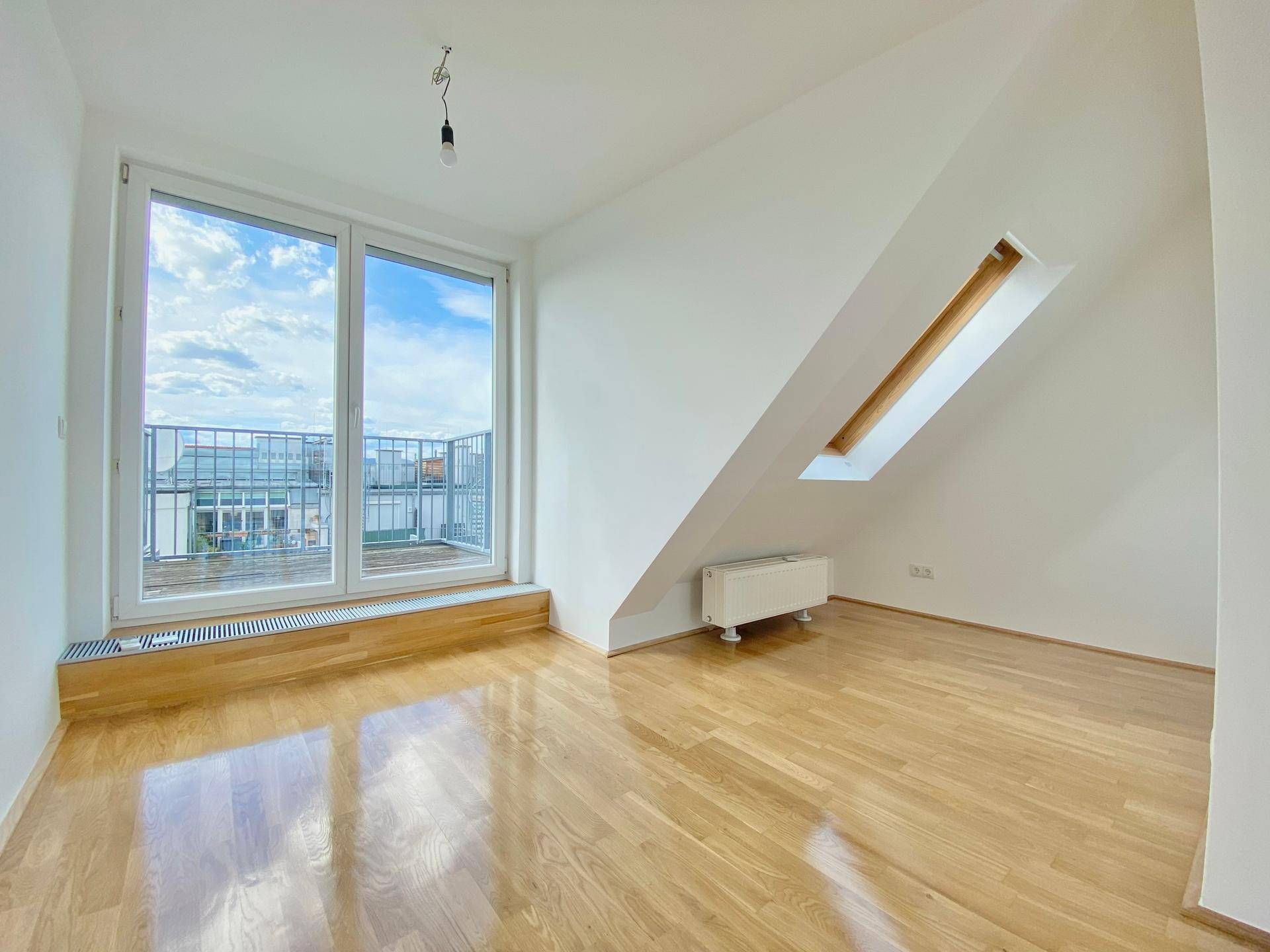 Helles Schlafzimmer mit Parkettboden und großem Fenster mit Zugang zum Balkon.