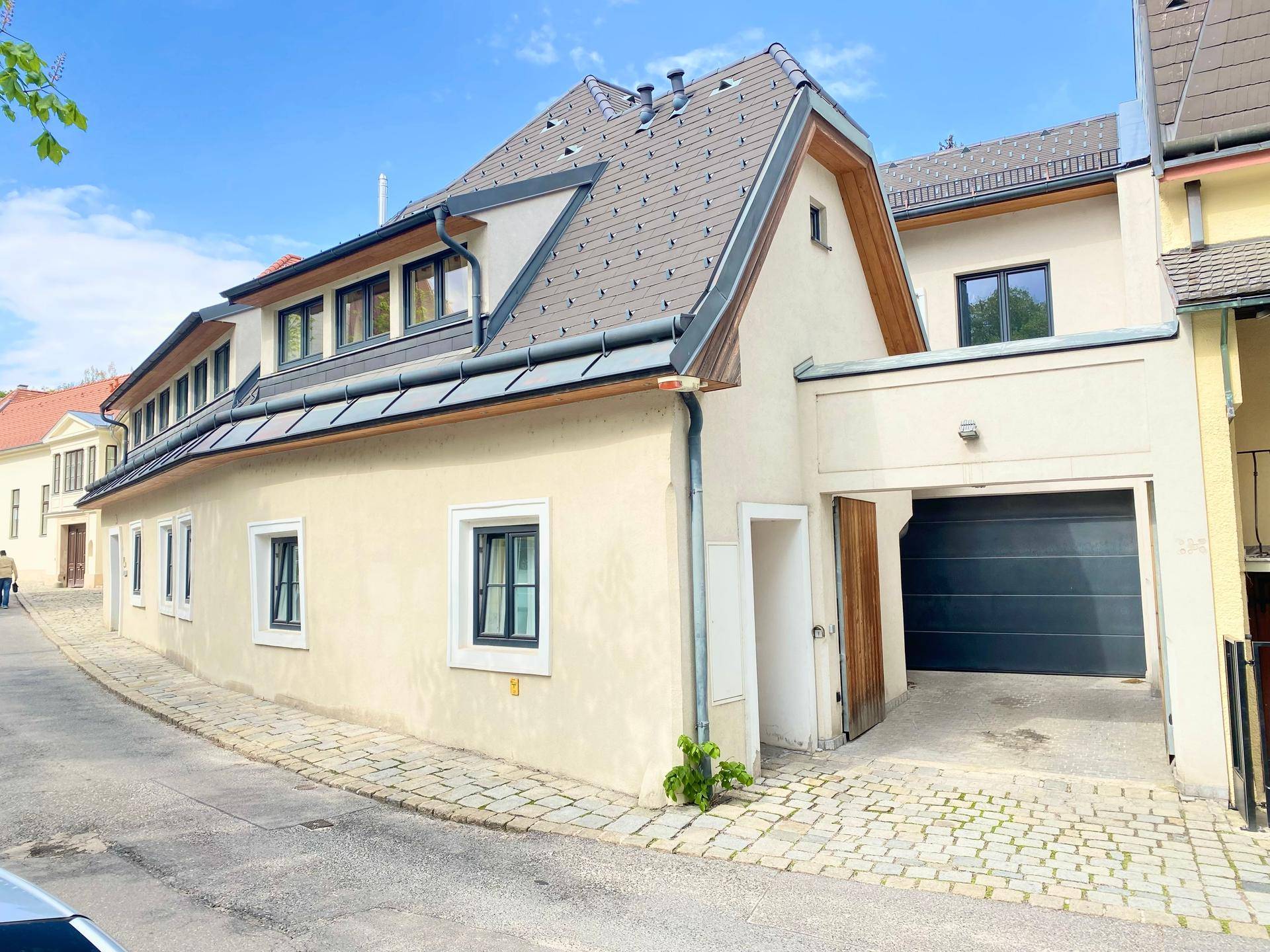 Außenansicht des Gebäudes mit Mansarddach und Garagenzufahrt von der Straße.