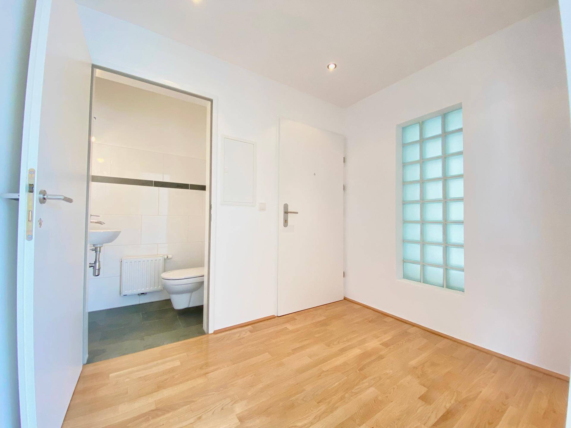 Heller Flur mit Parkettboden und Blick auf das Gäste-WC, ergänzt durch ein Glasbausteinfenster.