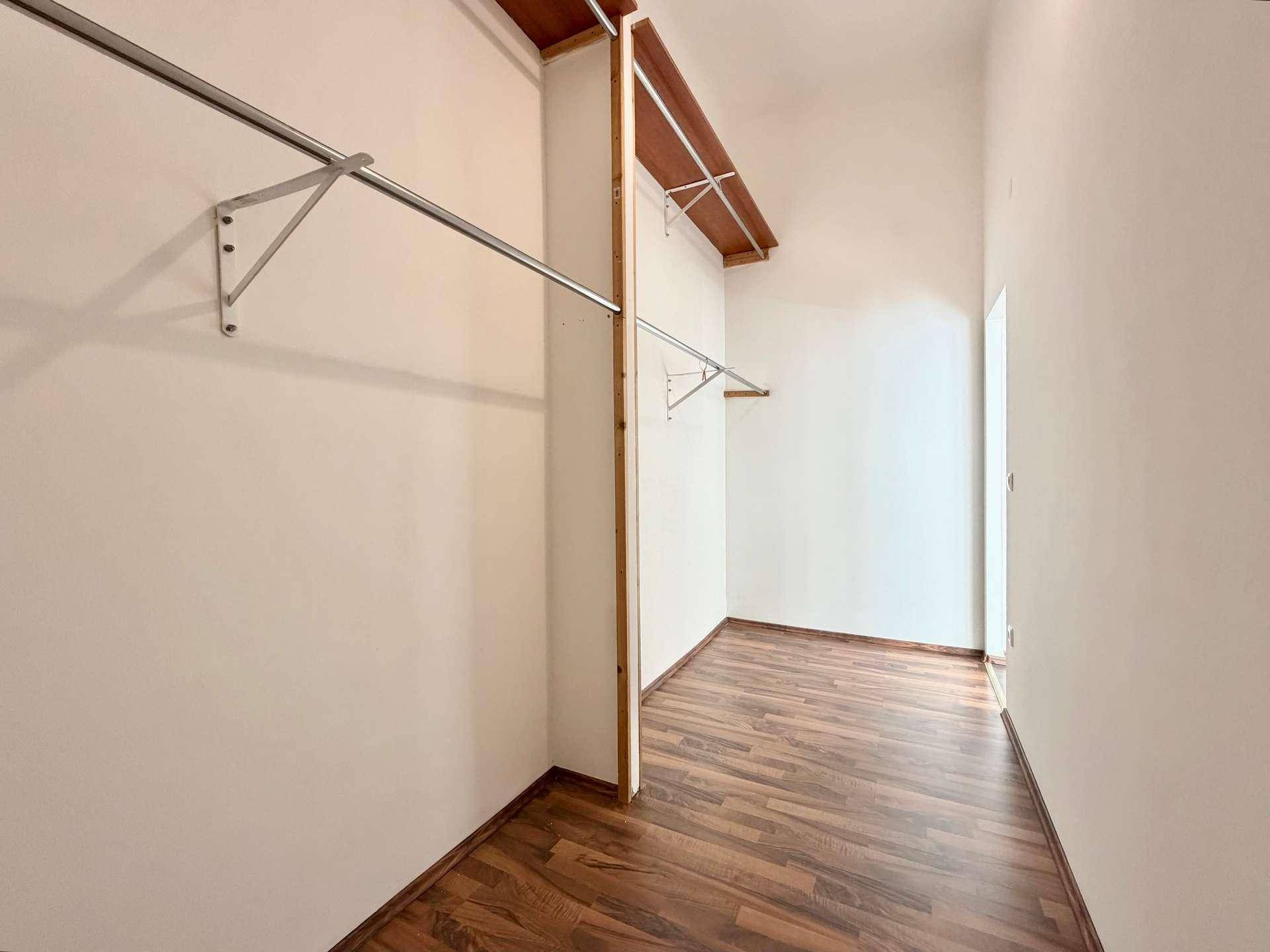 Geräumiger begehbarer Kleiderschrank mit Holzregalen und Metallstangen für Kleidung.