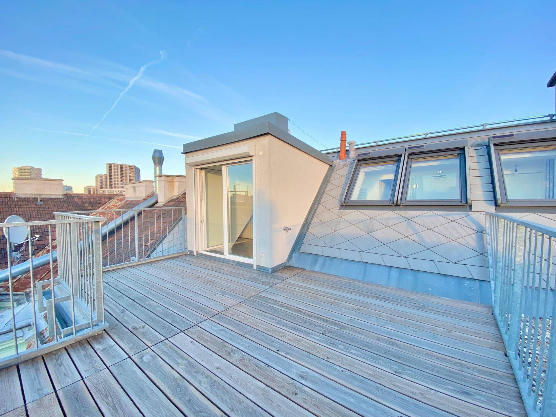 Geräumige Dachterrasse mit Holzbelag und Zugang zu einem Zimmer, bietet einen weiten Blick über die Stadt.