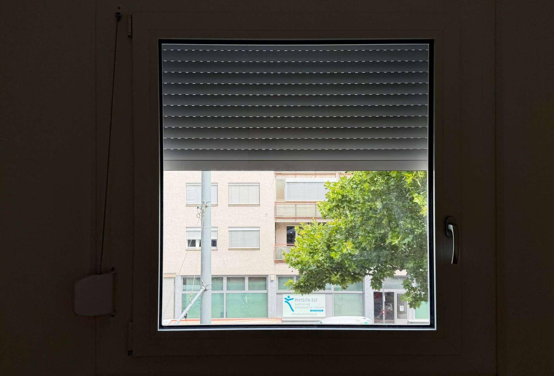 Fenster mit teilweise geschlossenem Rollladen, das einen Blick auf die Straße freigibt.