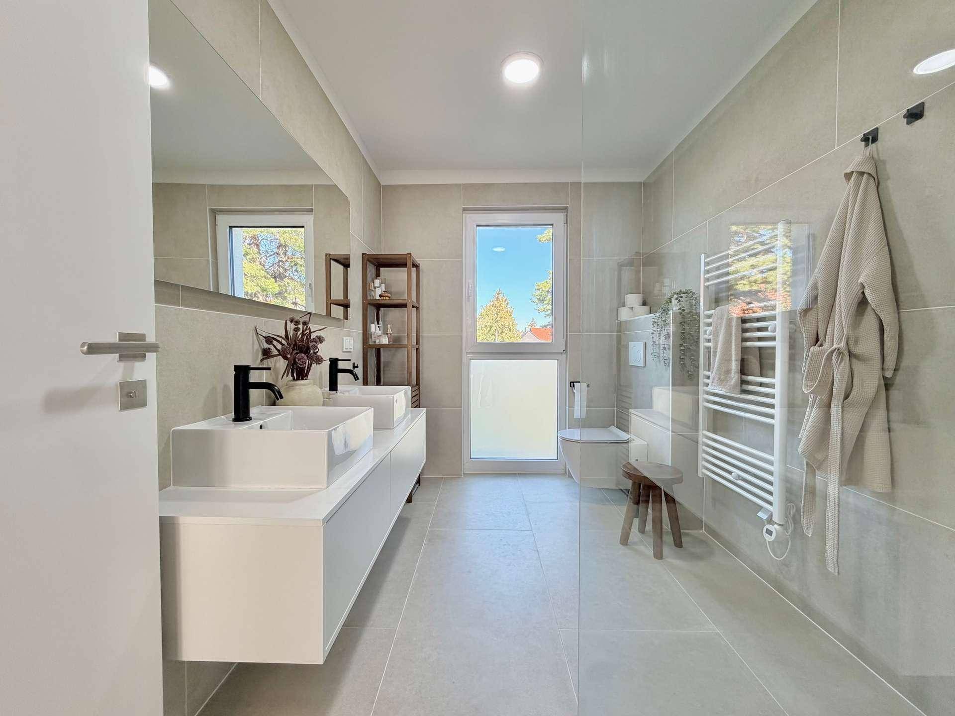 Modernes Badezimmer mit Doppelwaschbecken, großer Dusche und Fenster für Tageslicht.