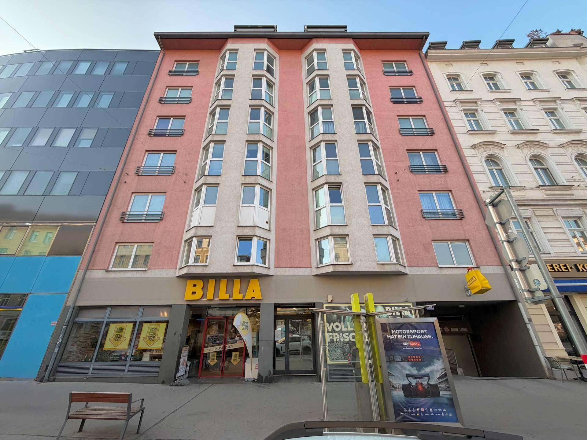 Mehrstöckiges Wohngebäude mit rosafarbener Fassade und einem Supermarkt im Erdgeschoss.