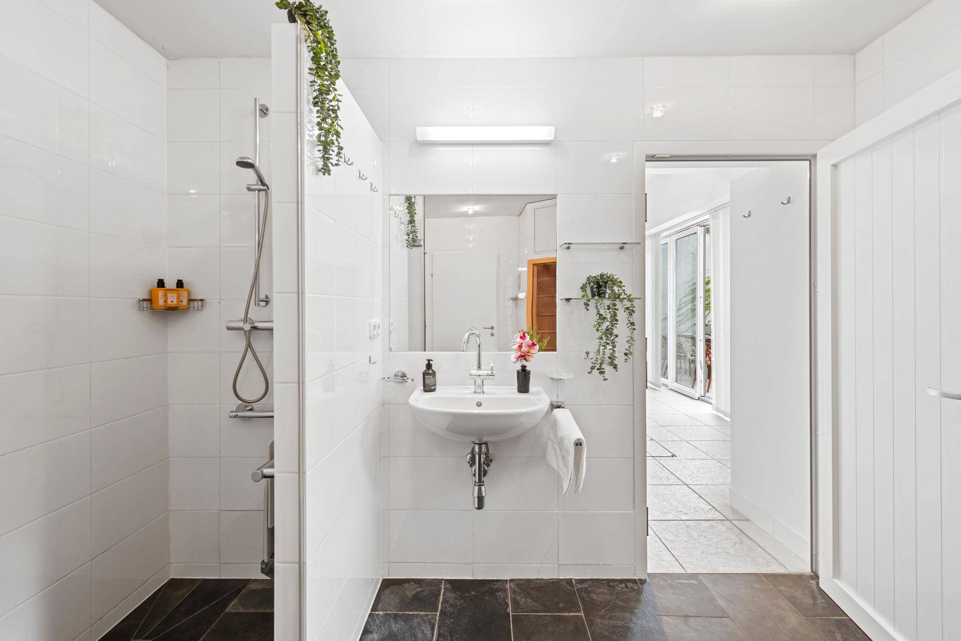 Modernes Badezimmer mit Dusche, Waschbecken und dunklem Fliesenboden.