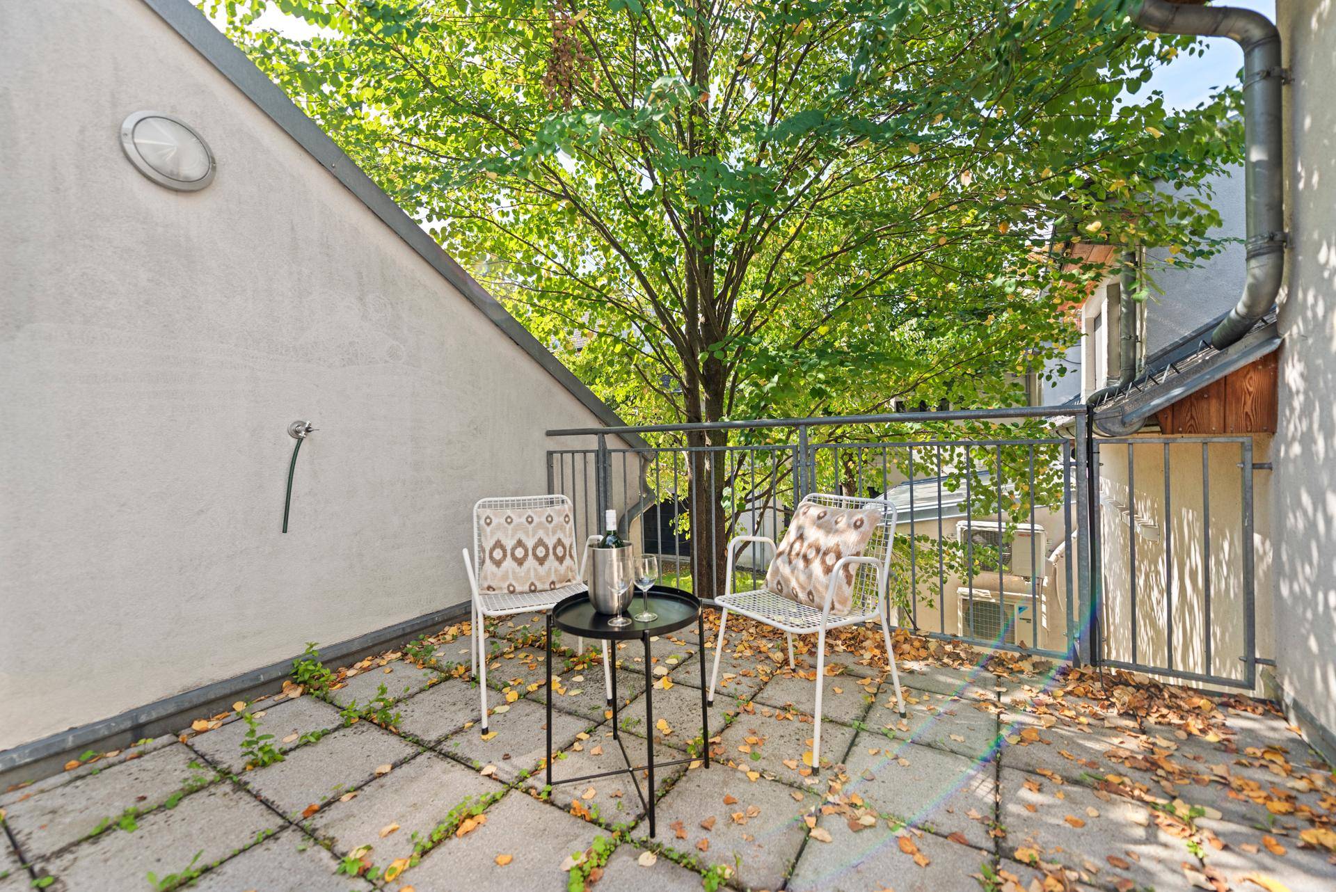 Kleiner Balkon mit Sitzgelegenheiten und Blick auf grüne Bäume.