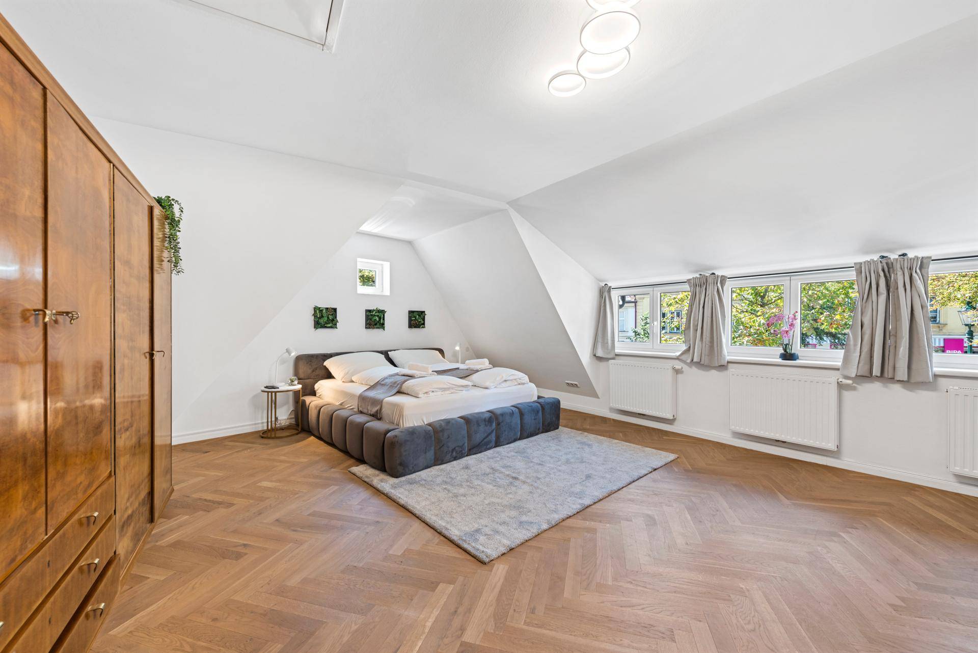 Geräumiges Schlafzimmer im Dachgeschoss mit Holzkleiderschrank und Blick aus den Fenstern.