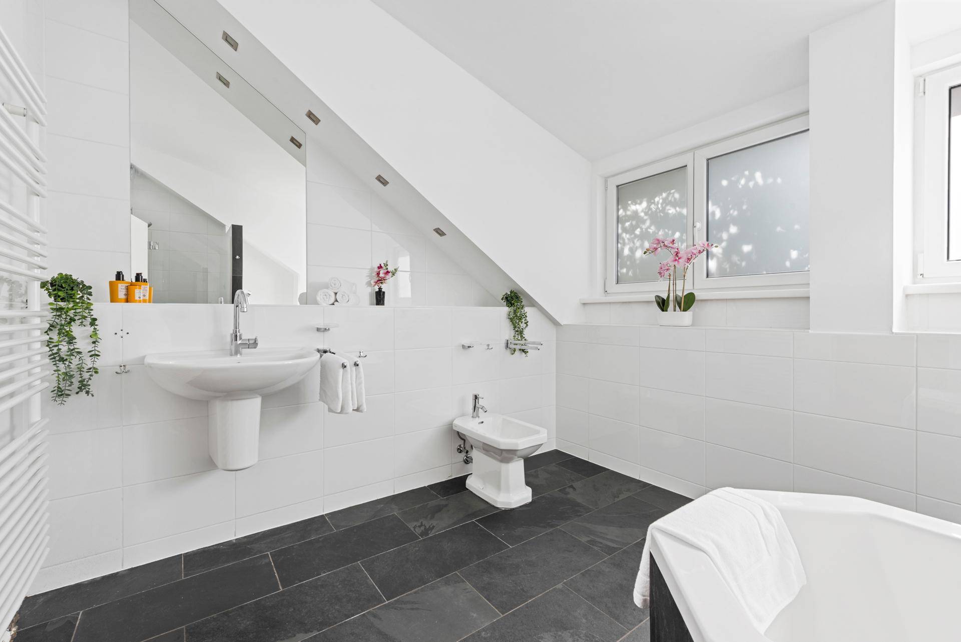 Helles Badezimmer mit Waschbecken, Bidet, Badewanne und beheiztem Handtuchhalter.