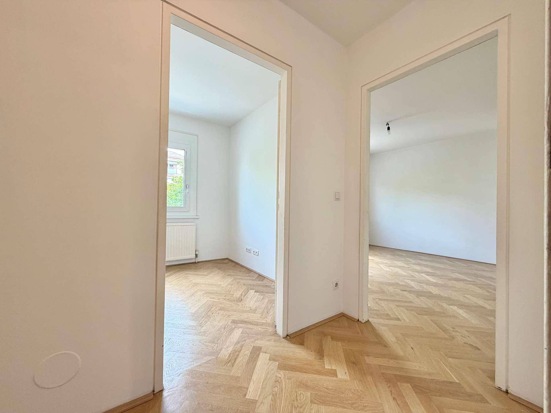 Blick vom Flur in zwei helle, leere Zimmer mit durchgehendem Fischgrätparkettboden.