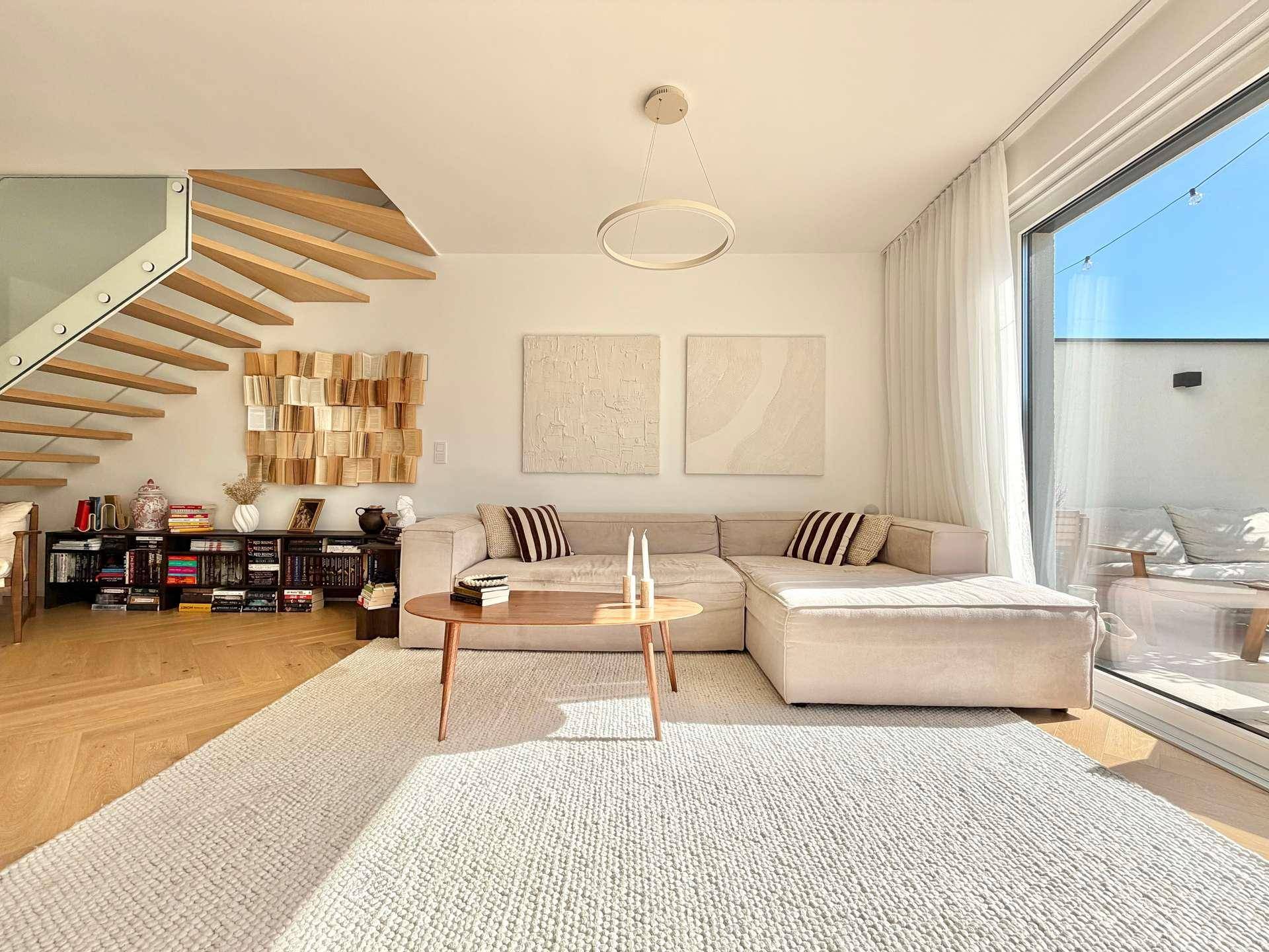 Heller Wohnbereich mit beigem Sofa, moderner Treppe und direktem Zugang zum Garten.
