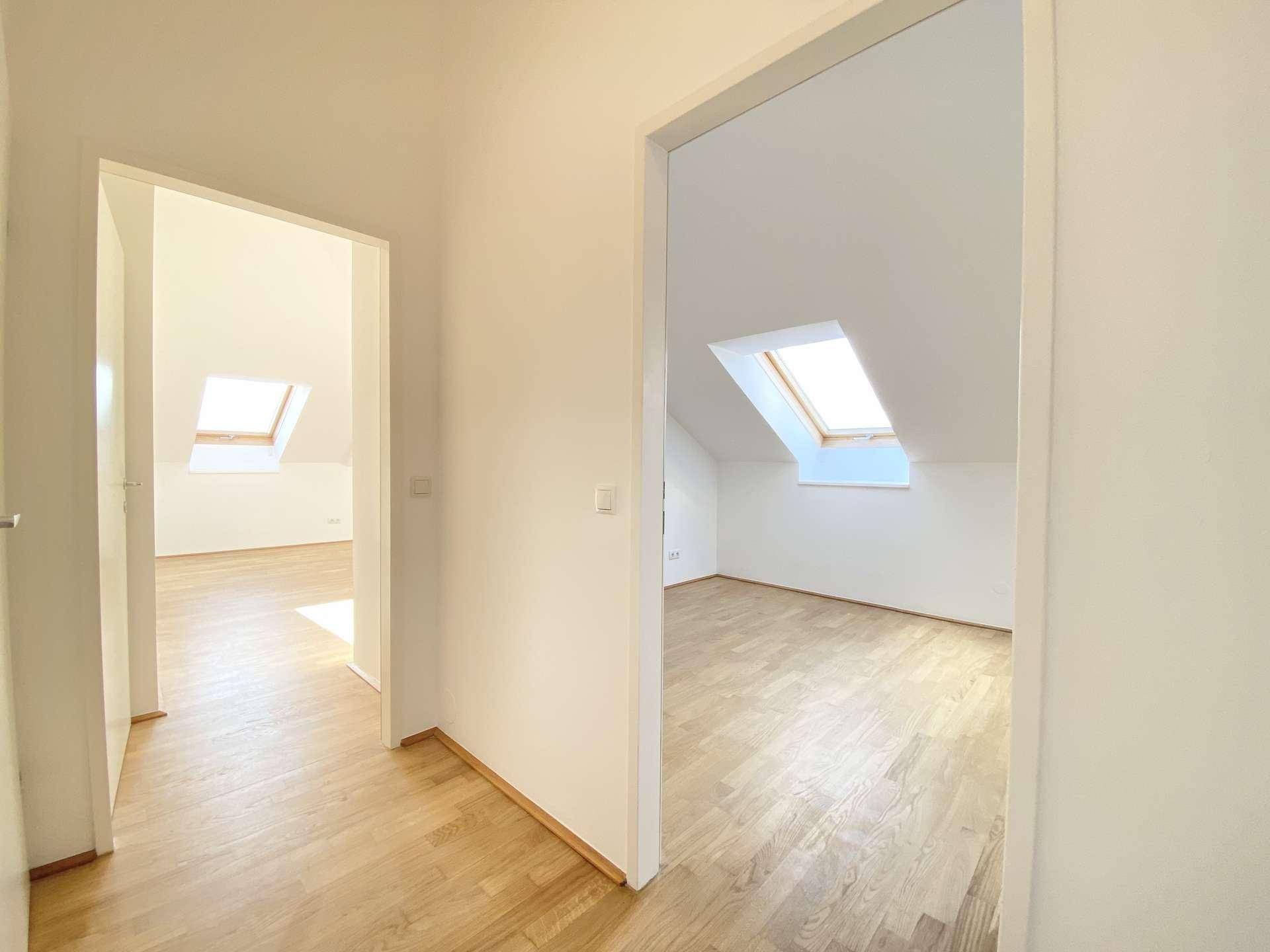 Blick in zwei helle Zimmer mit Holzfußboden und Dachfenstern, die viel Licht spenden.