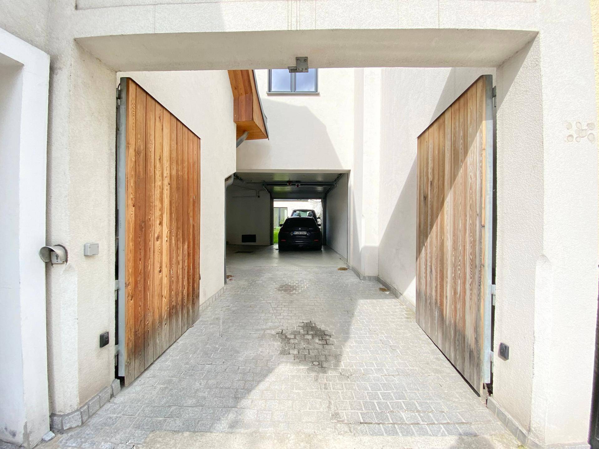 Einfahrt zur Garage mit Holztoren und gepflastertem Zugangsbereich.