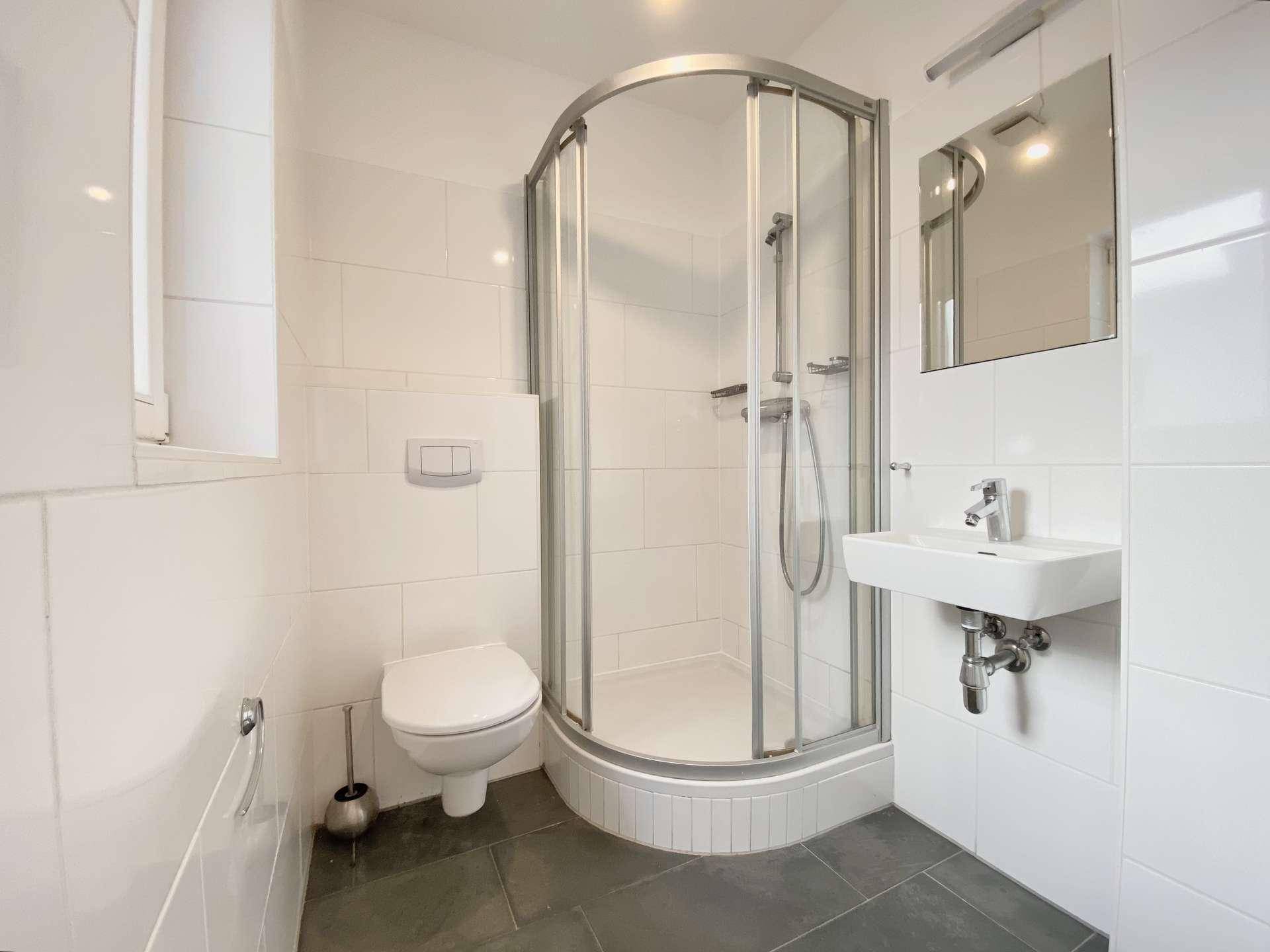 Kleines Badezimmer mit Duschkabine, WC und Waschbecken, hell gefliest.