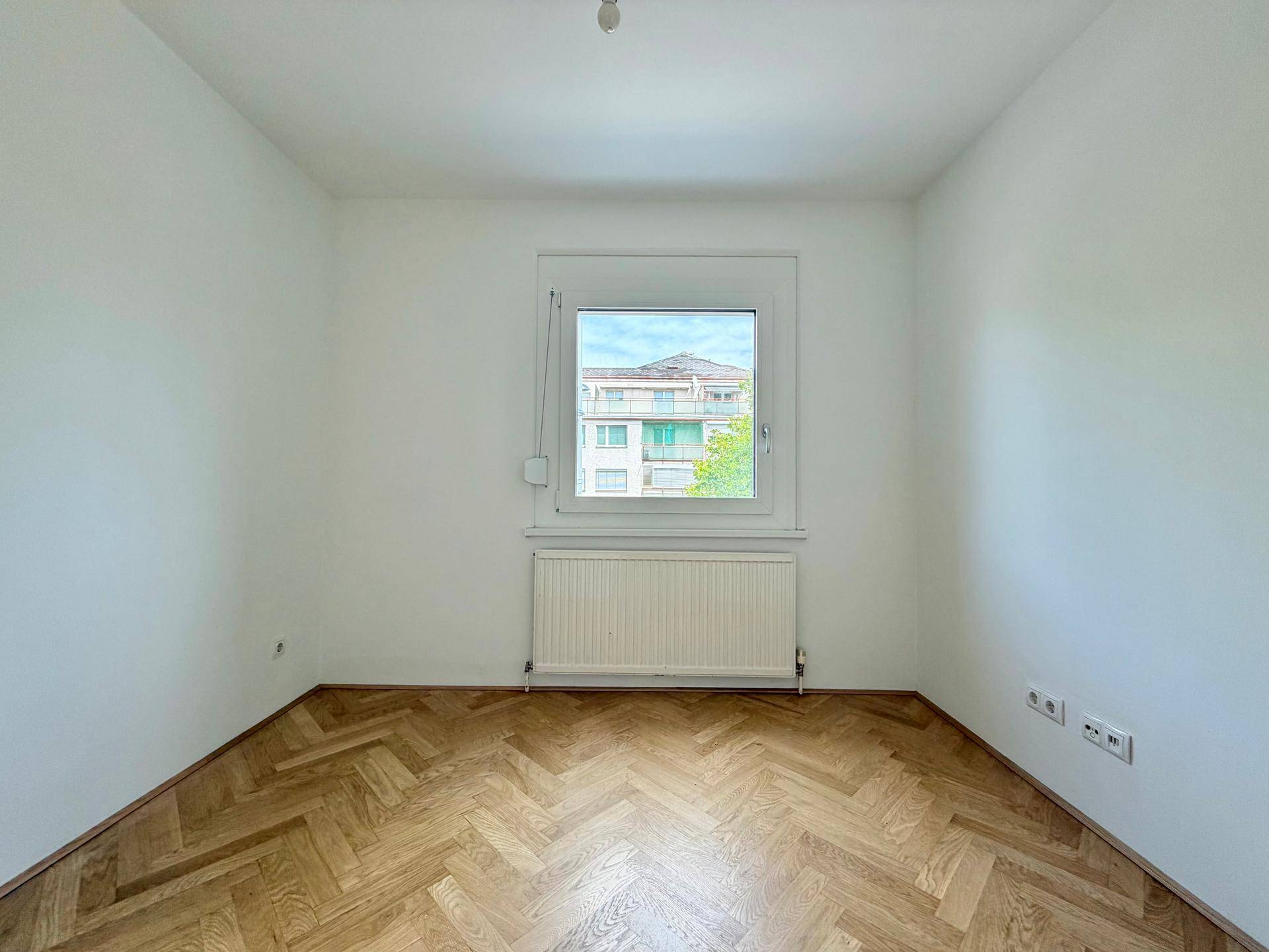 Leeres Zimmer mit Fischgrätparkett und einem Fenster, das eine angenehme Atmosphäre schafft.