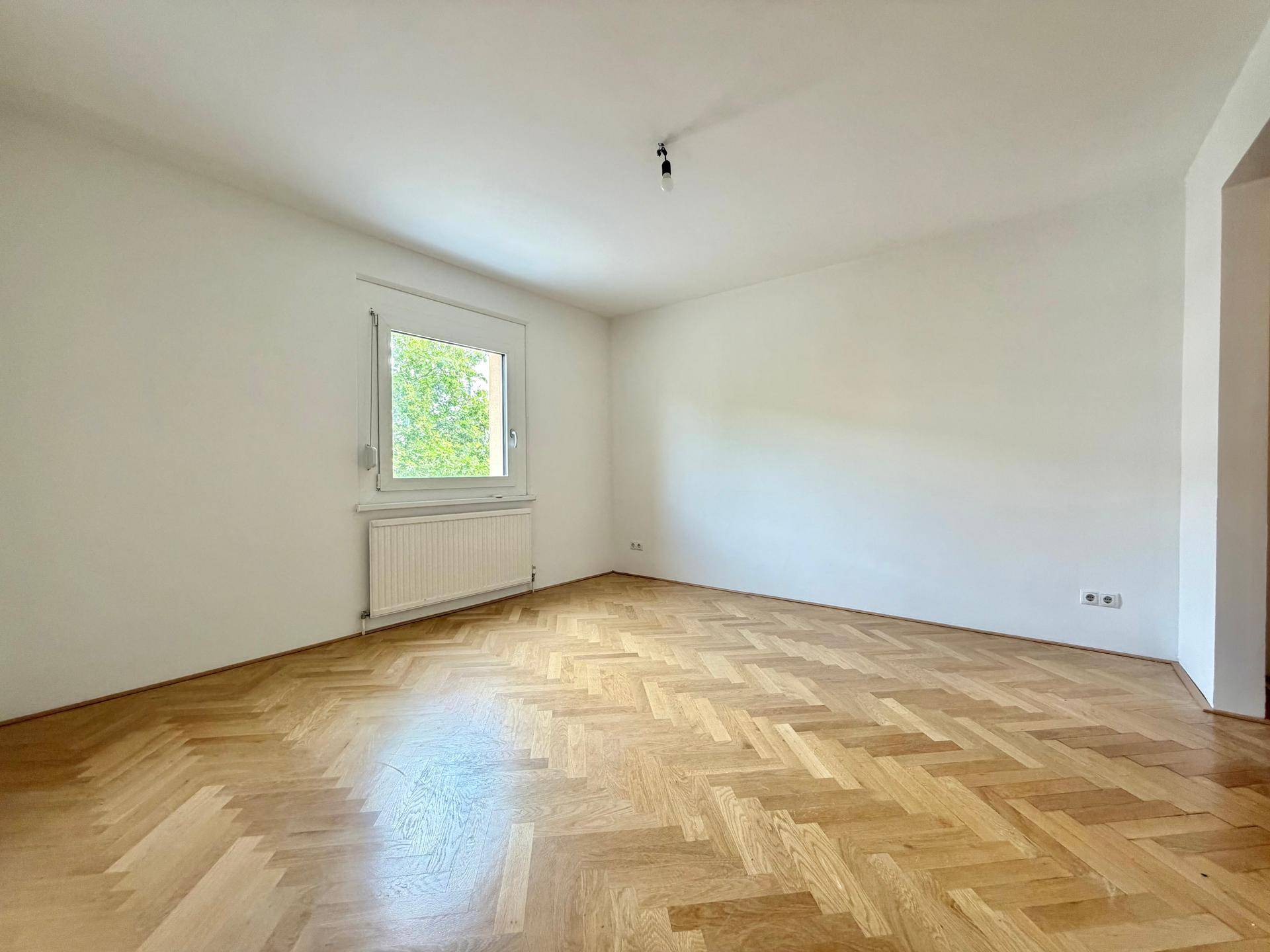 Helles und geräumiges Zimmer mit Fischgrätparkett und einem Fenster, das viel Licht spendet.