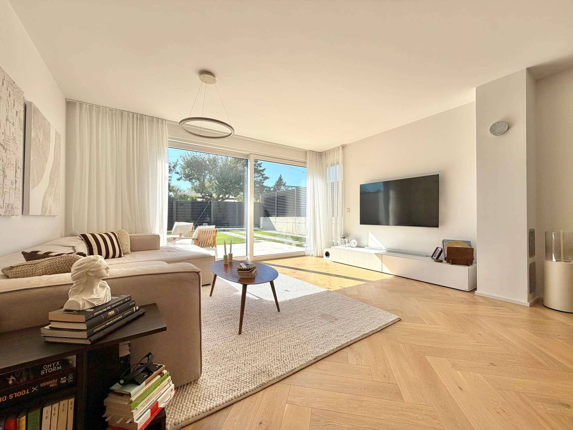 Helles Wohnzimmer mit beigem Ecksofa, Couchtisch und großem Fenster zum Garten.