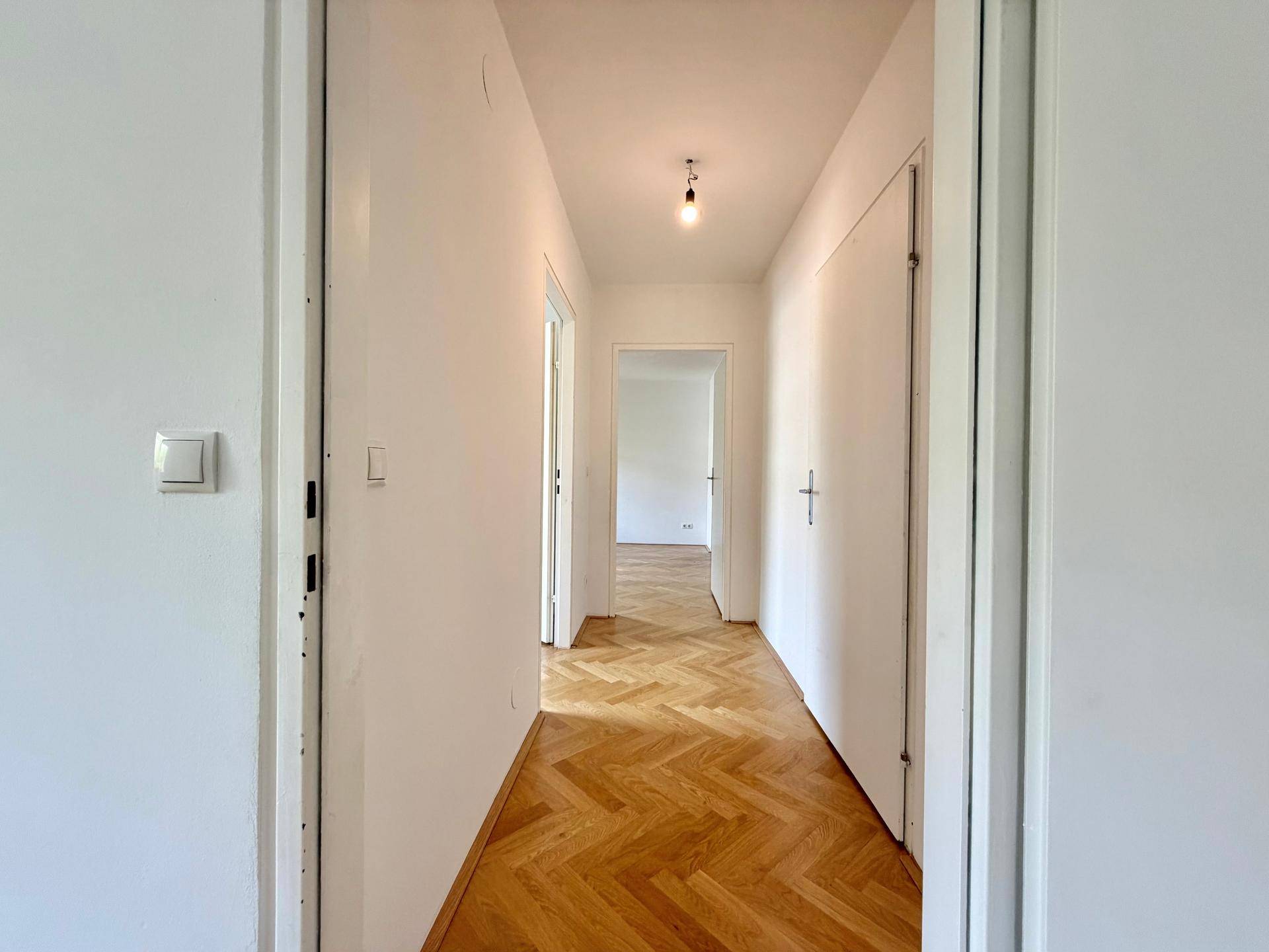 Heller Flur mit Fischgrätparkett, der zu verschiedenen Wohnbereichen der Immobilie führt.