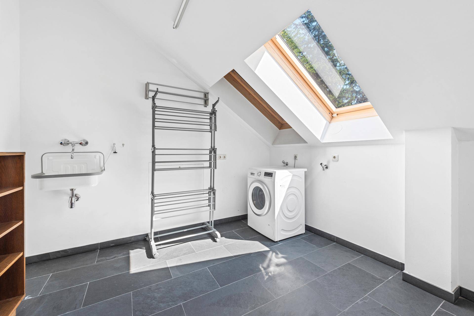 Praktischer Hauswirtschaftsraum mit Waschmaschine, Waschbecken und Dachfenster für Tageslicht.