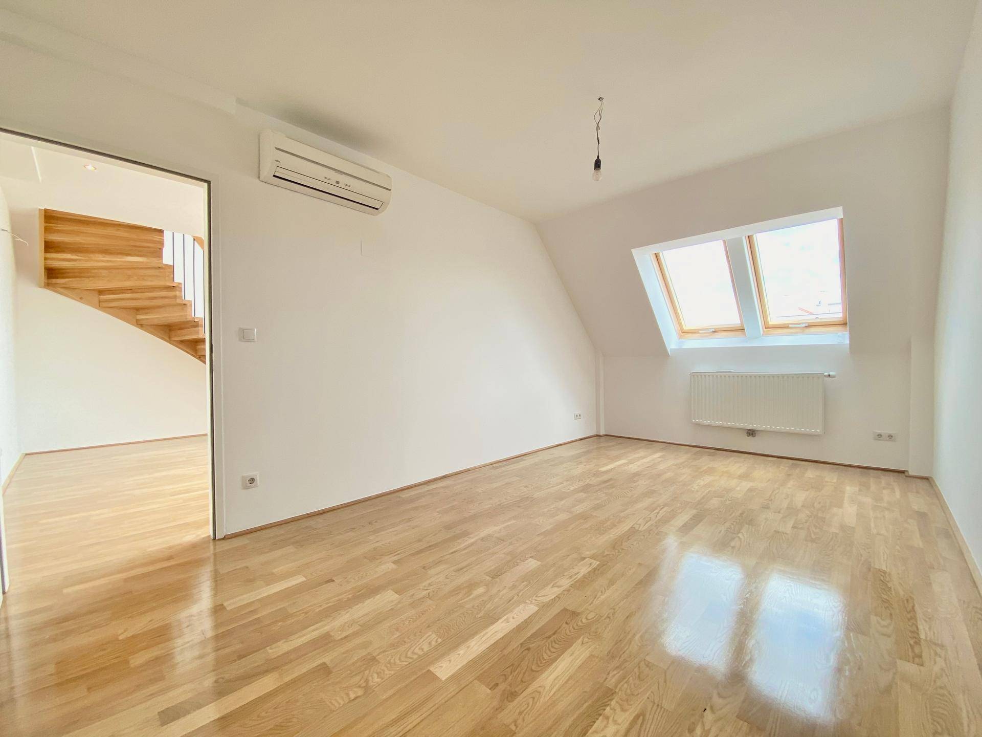 Geräumiger Wohnraum mit Parkettboden, Klimaanlage und Dachfenstern für natürliche Belichtung.