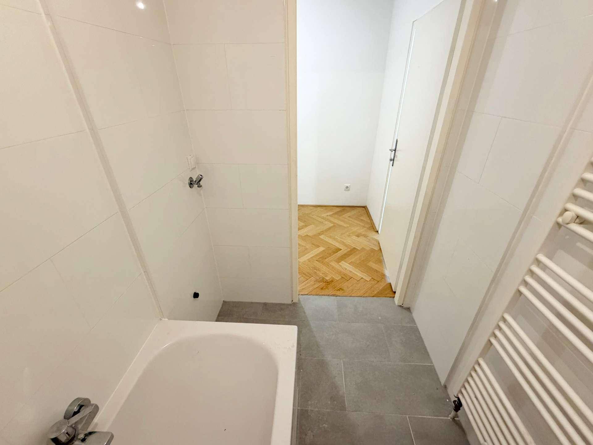 Blick aus dem Badezimmer in den angrenzenden Raum mit Fischgrätparkettboden.