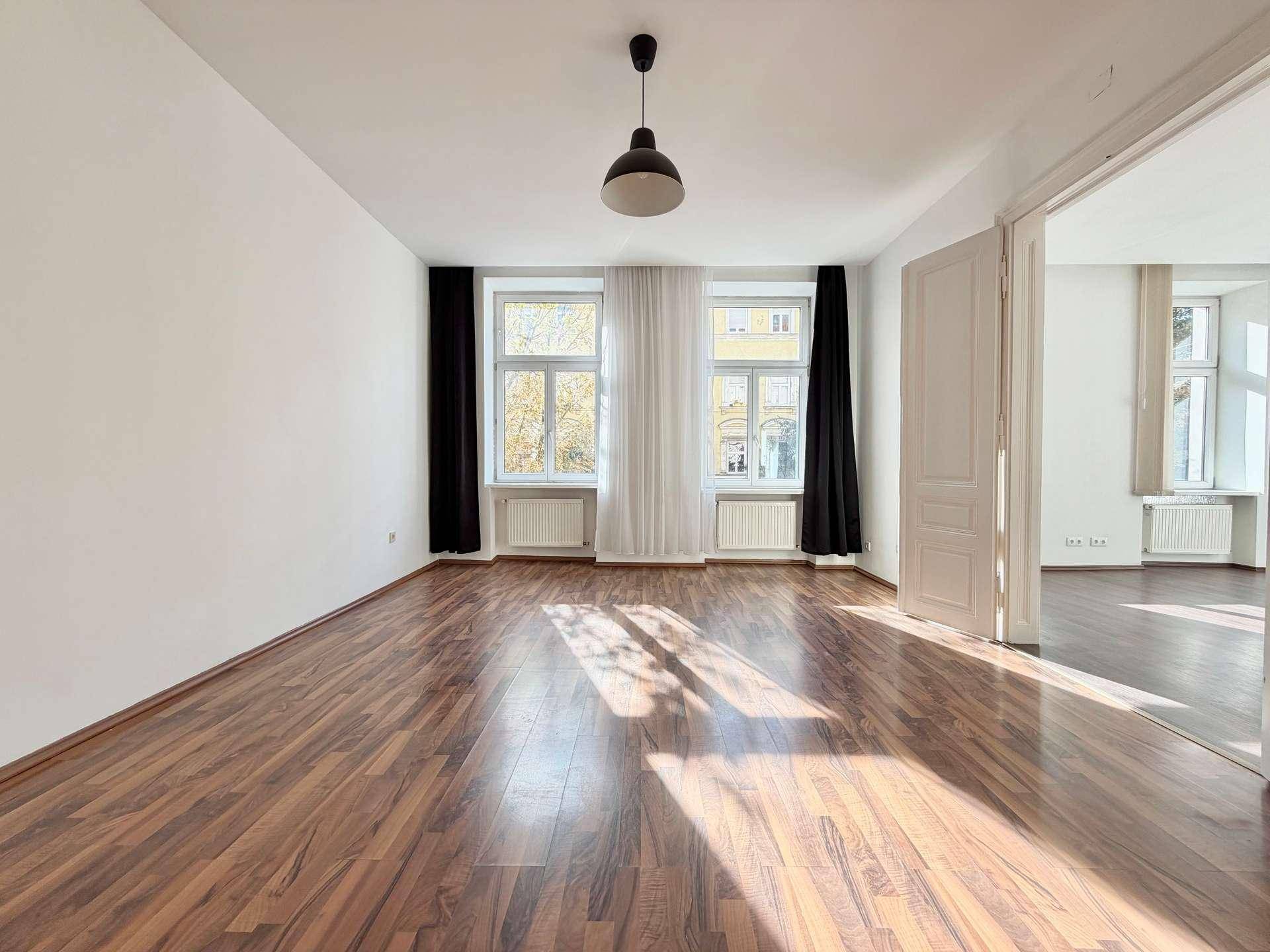Lichtdurchflutetes Wohnzimmer mit dunklem Laminatboden und Blick auf die umliegenden Gebäude.