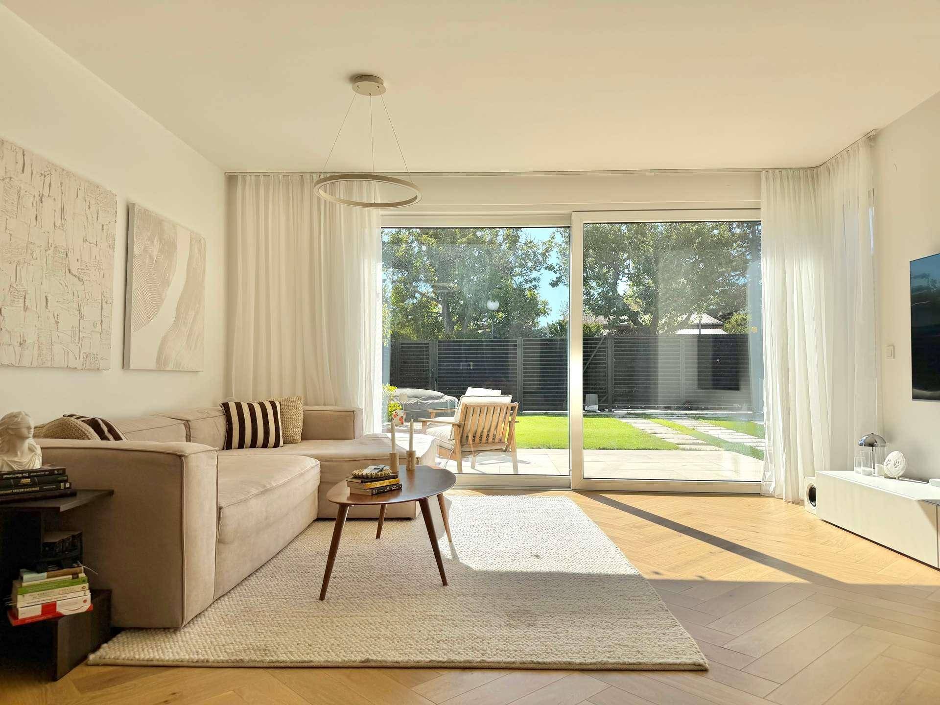 Gemütliches Wohnzimmer mit beigem Sofa und weitem Blick durch die großen Fenster in den Garten.
