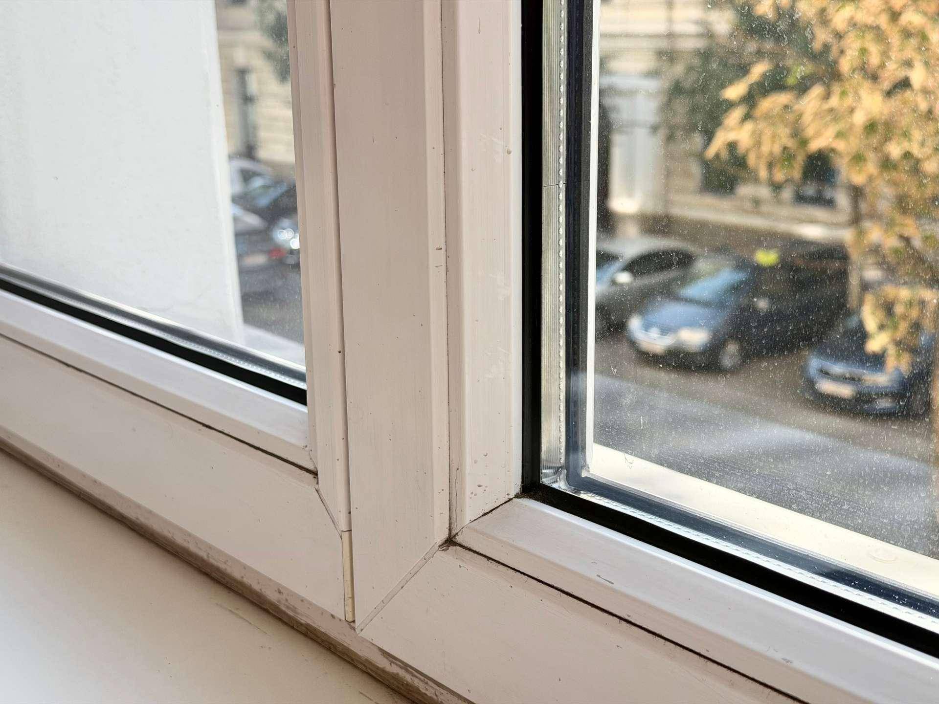 Nahaufnahme eines weißen Fensterrahmens mit Blick auf die Straße und parkende Autos.