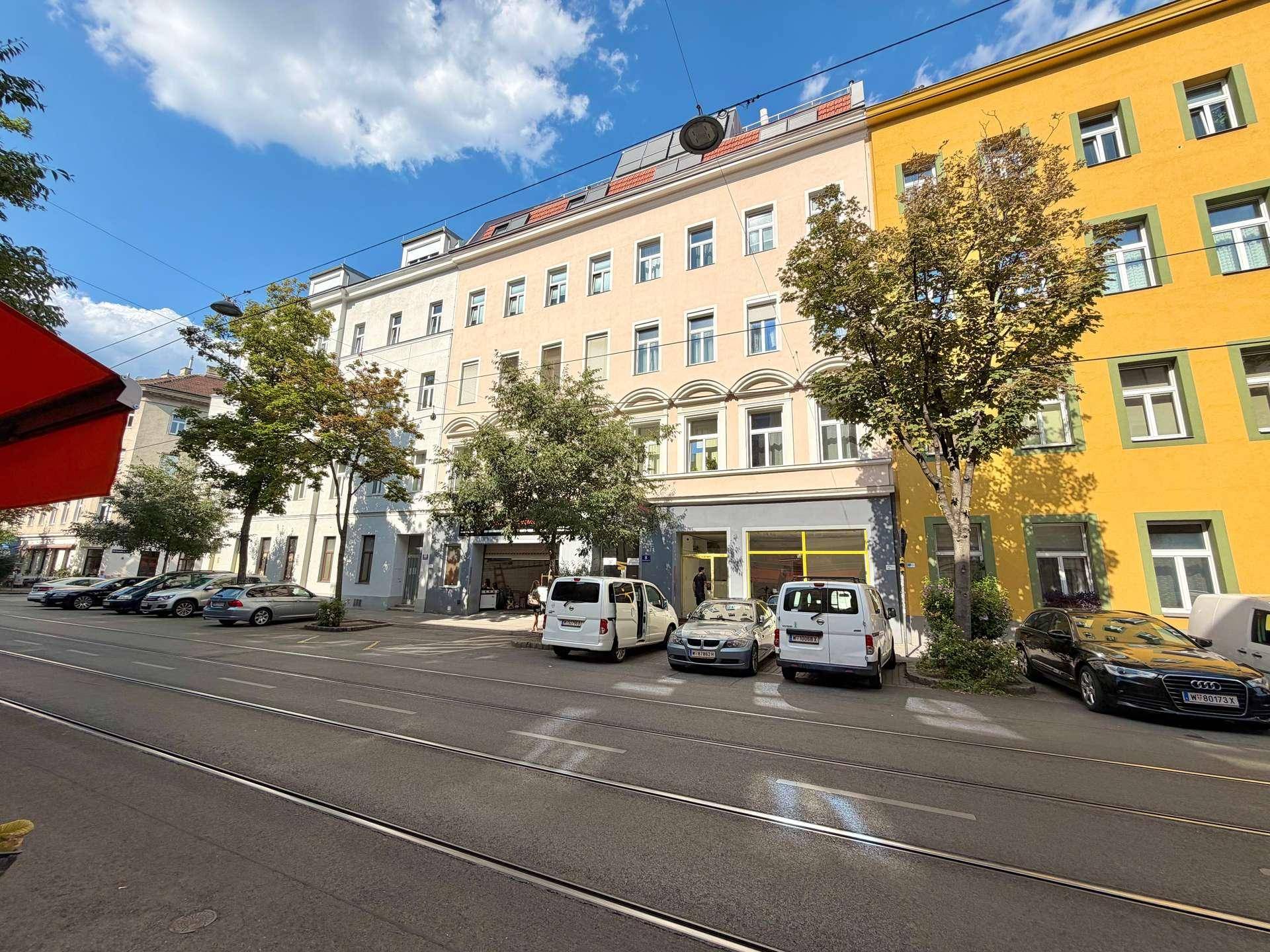 Straßenansicht eines Mehrfamilienhauses mit parkenden Autos und Bäumen entlang der Straße.