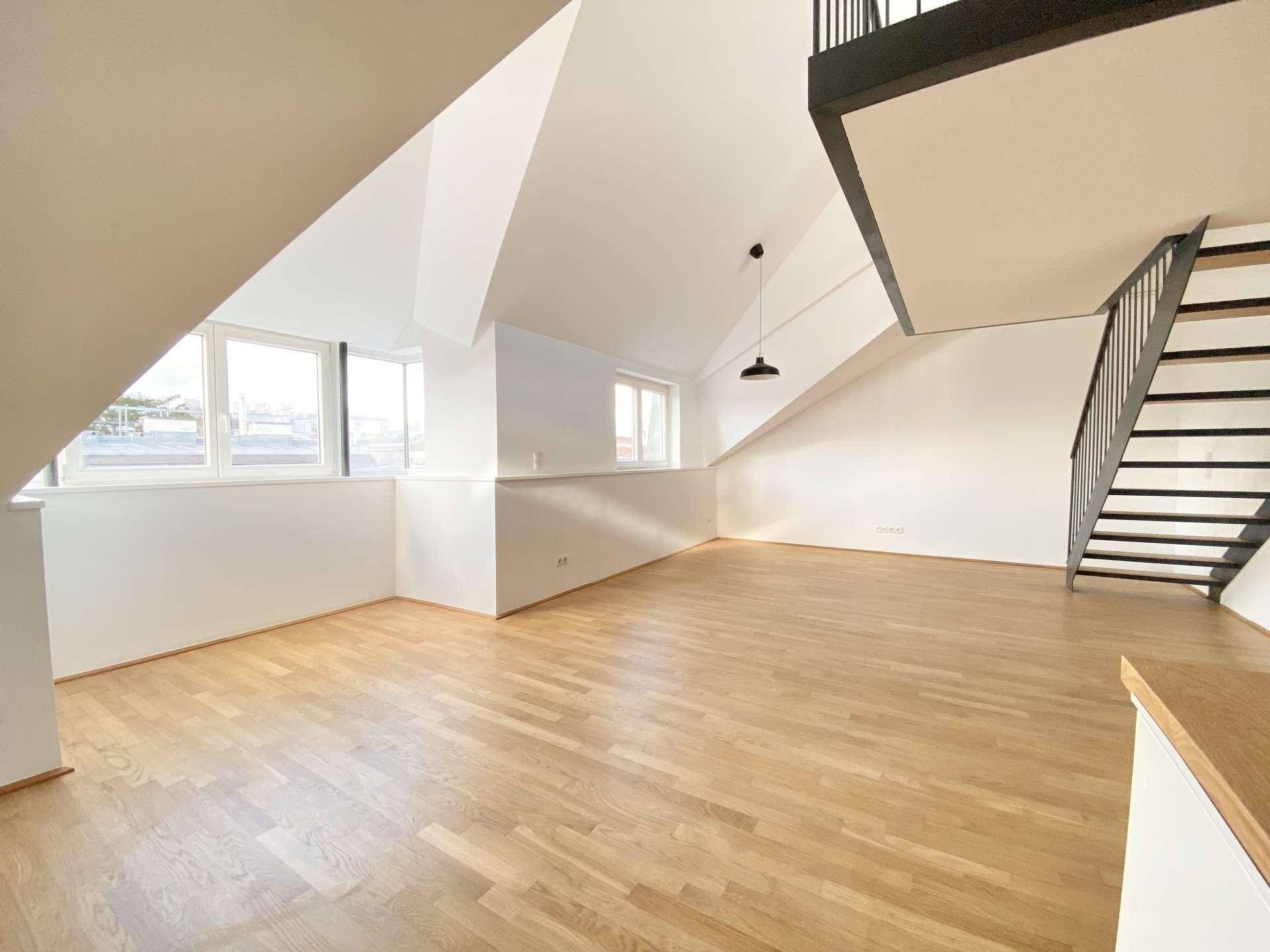 Geräumiger Wohnbereich mit Holzboden, großen Fenstern und moderner Treppe zum Obergeschoss.