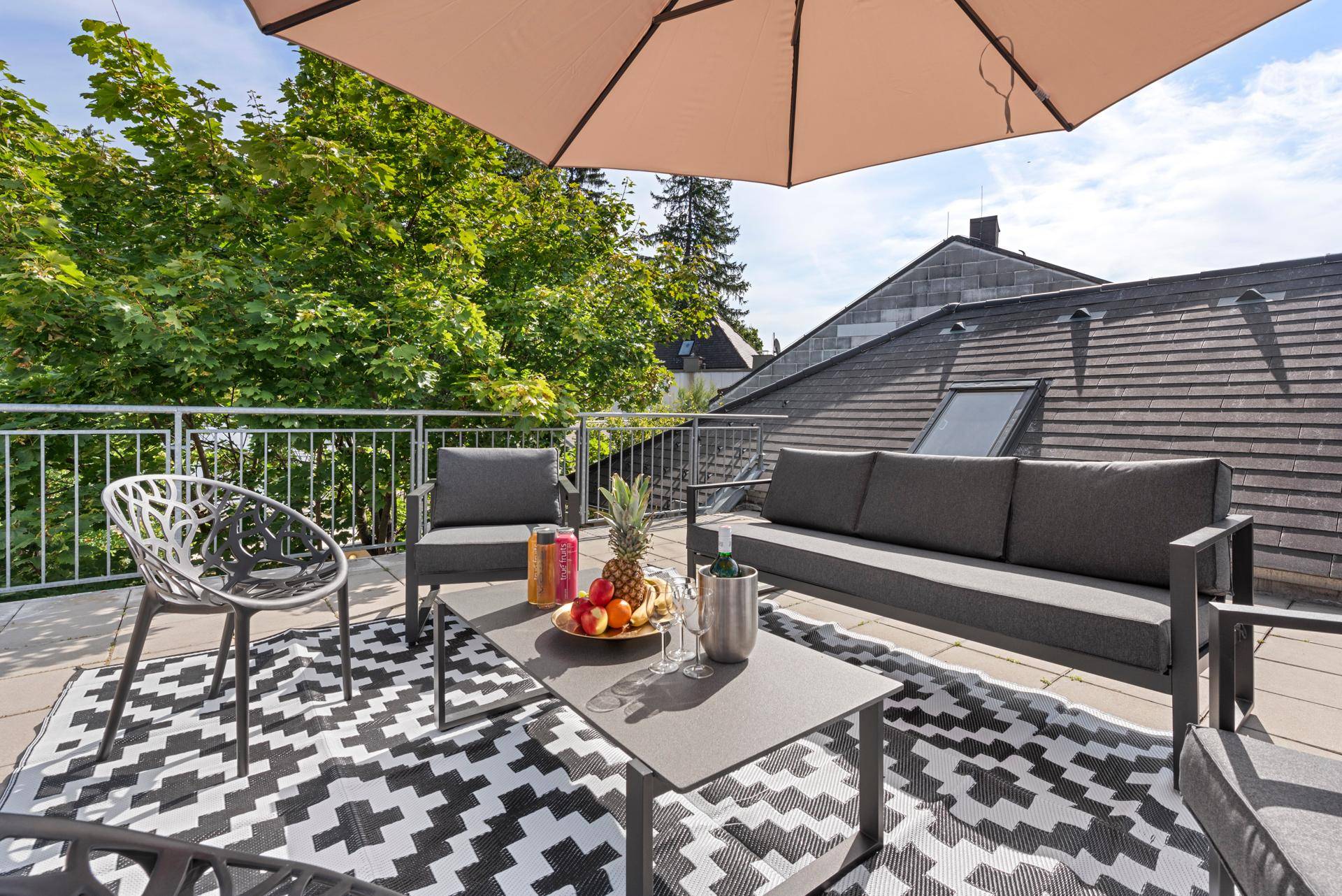Detailansicht der Dachterrasse mit bequemen Sitzgelegenheiten und Sonnenschirm.