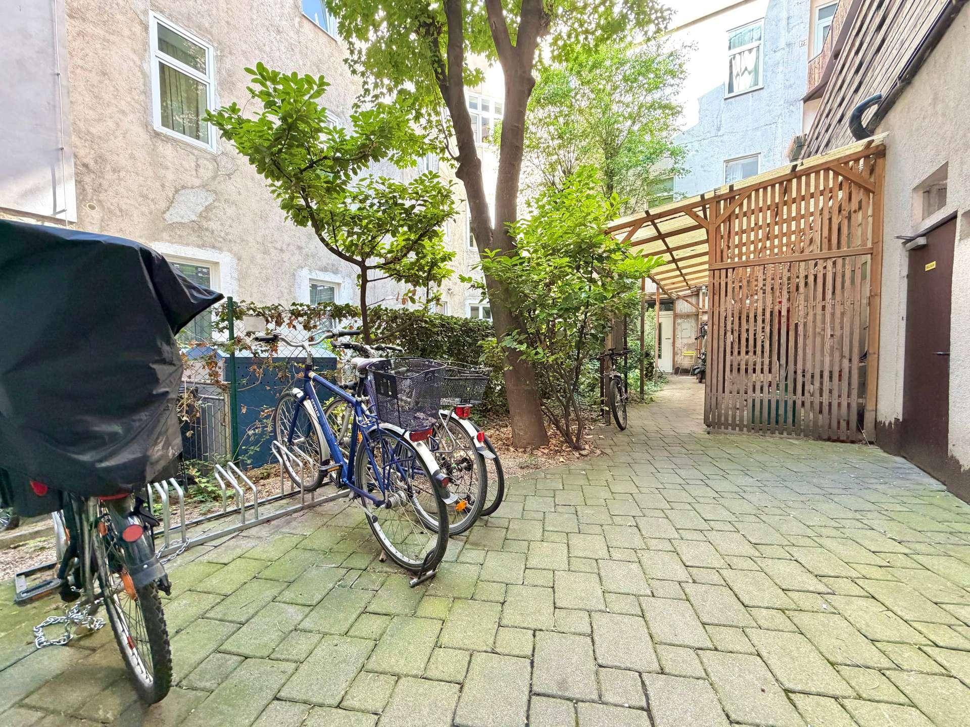 Gepflasterter Innenhof mit Fahrradabstellplätzen und grünen Bäumen, umgeben von Gebäuden.