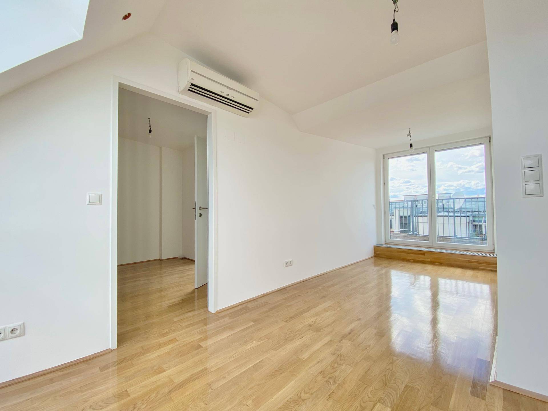 Geräumiger Wohnbereich mit Parkettboden, Klimaanlage und Zugang zu einem sonnigen Balkon.