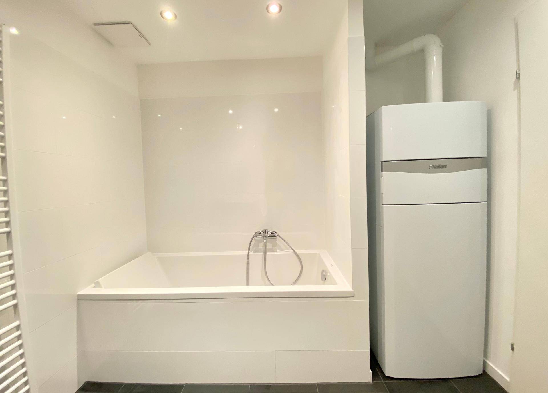 Badezimmer mit Badewanne und integriertem Warmwasserbereiter, modern gefliest.