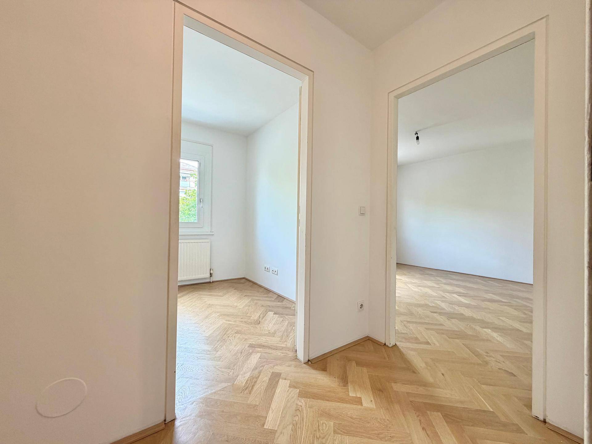Blick vom Flur in zwei helle, leere Zimmer mit Fischgrätparkett, die viel Potenzial bieten.