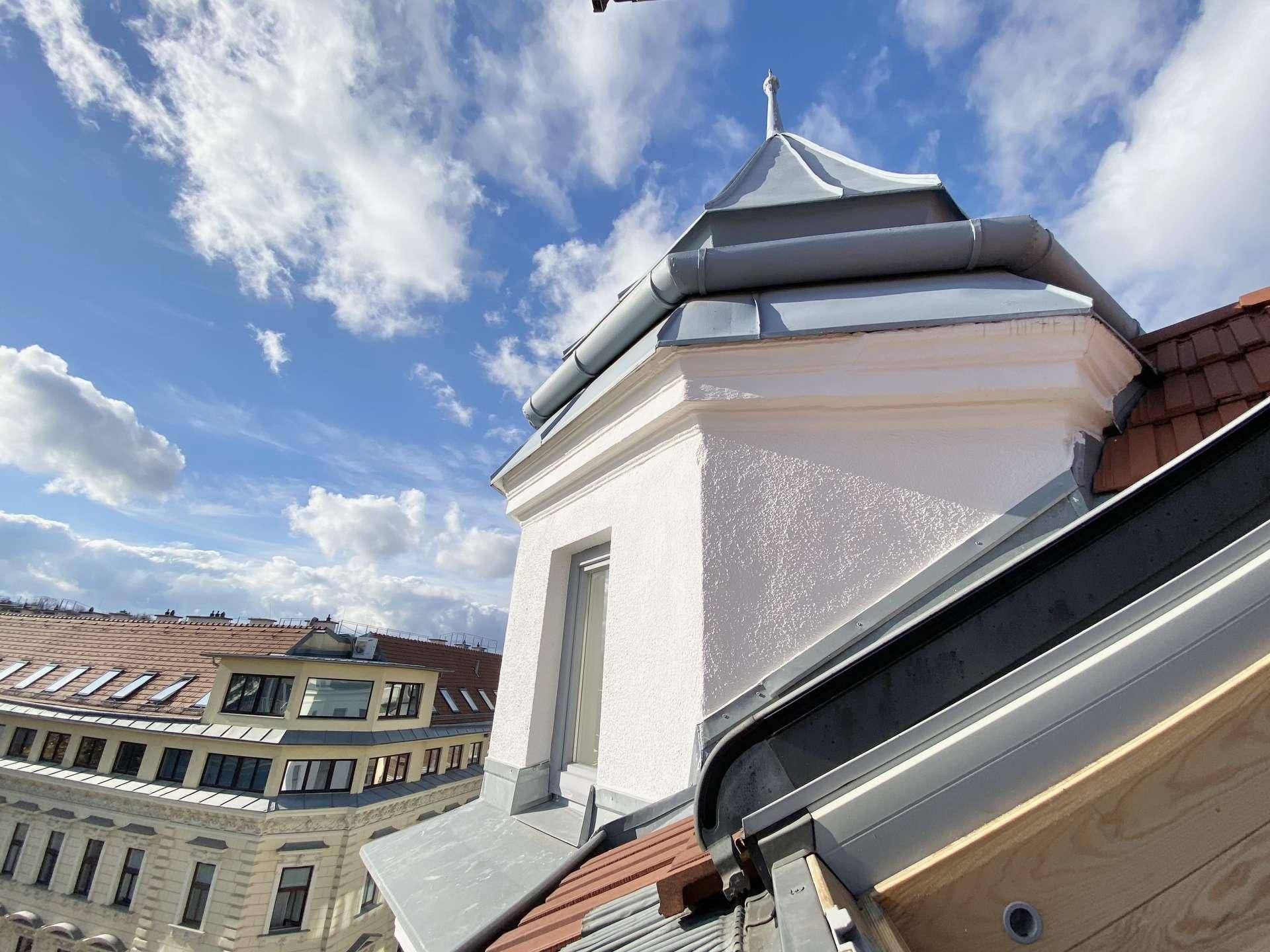 Historisches Dachdetail mit Gaube und Ziegeldach unter einem blauen Himmel.