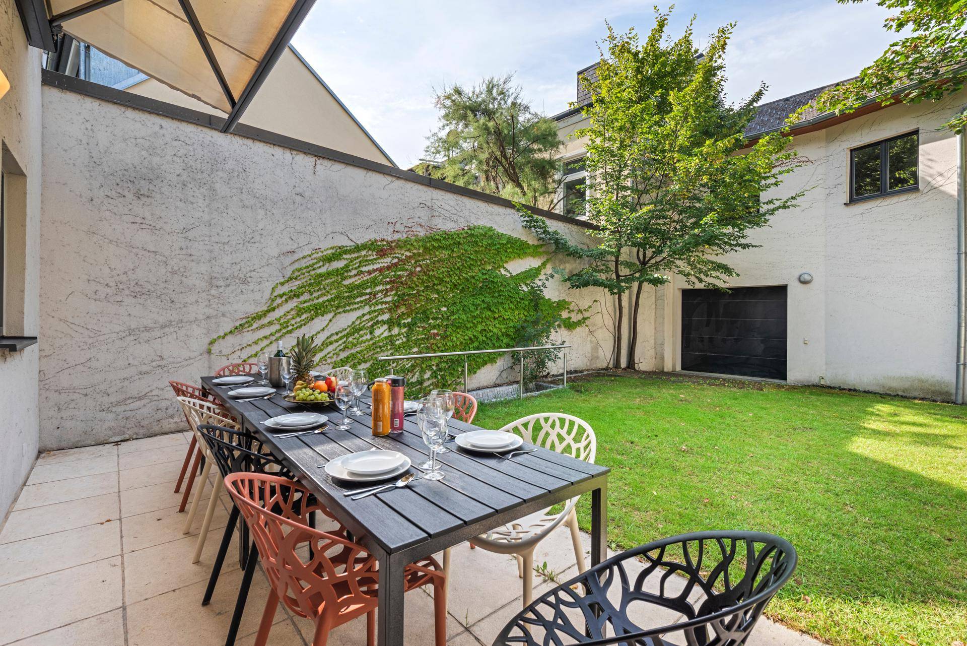 Möblierte Terrasse mit Esstisch und Stühlen, umgeben von Rasen und Grünflächen.