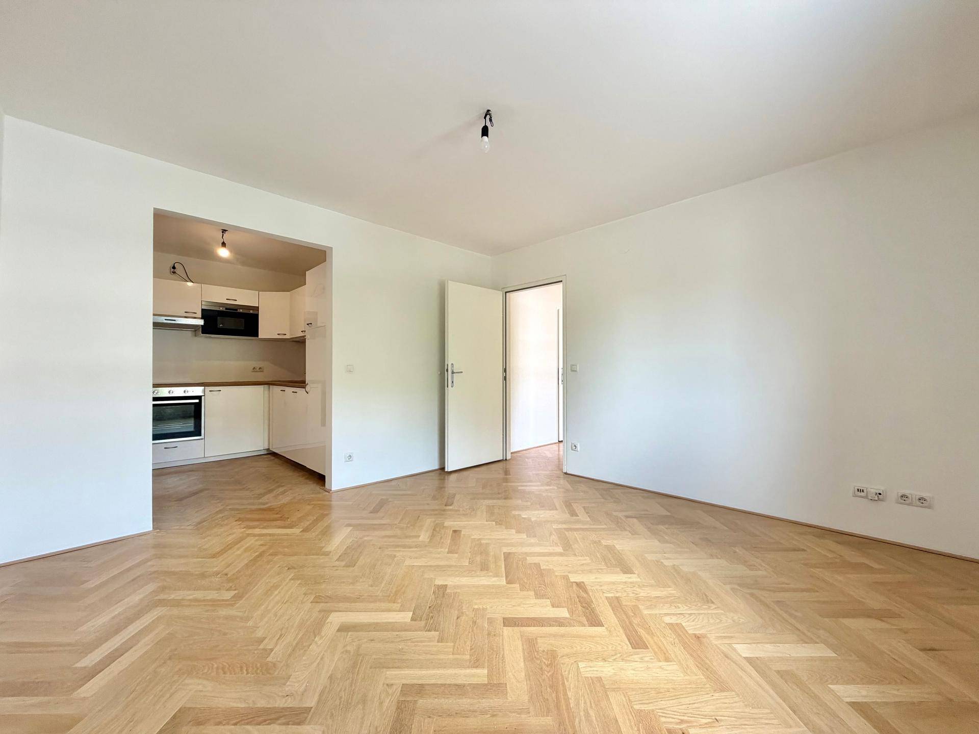 Heller Wohnbereich mit Fischgrätparkett und integrierter Küchenzeile, ideal für offenes Wohnen.