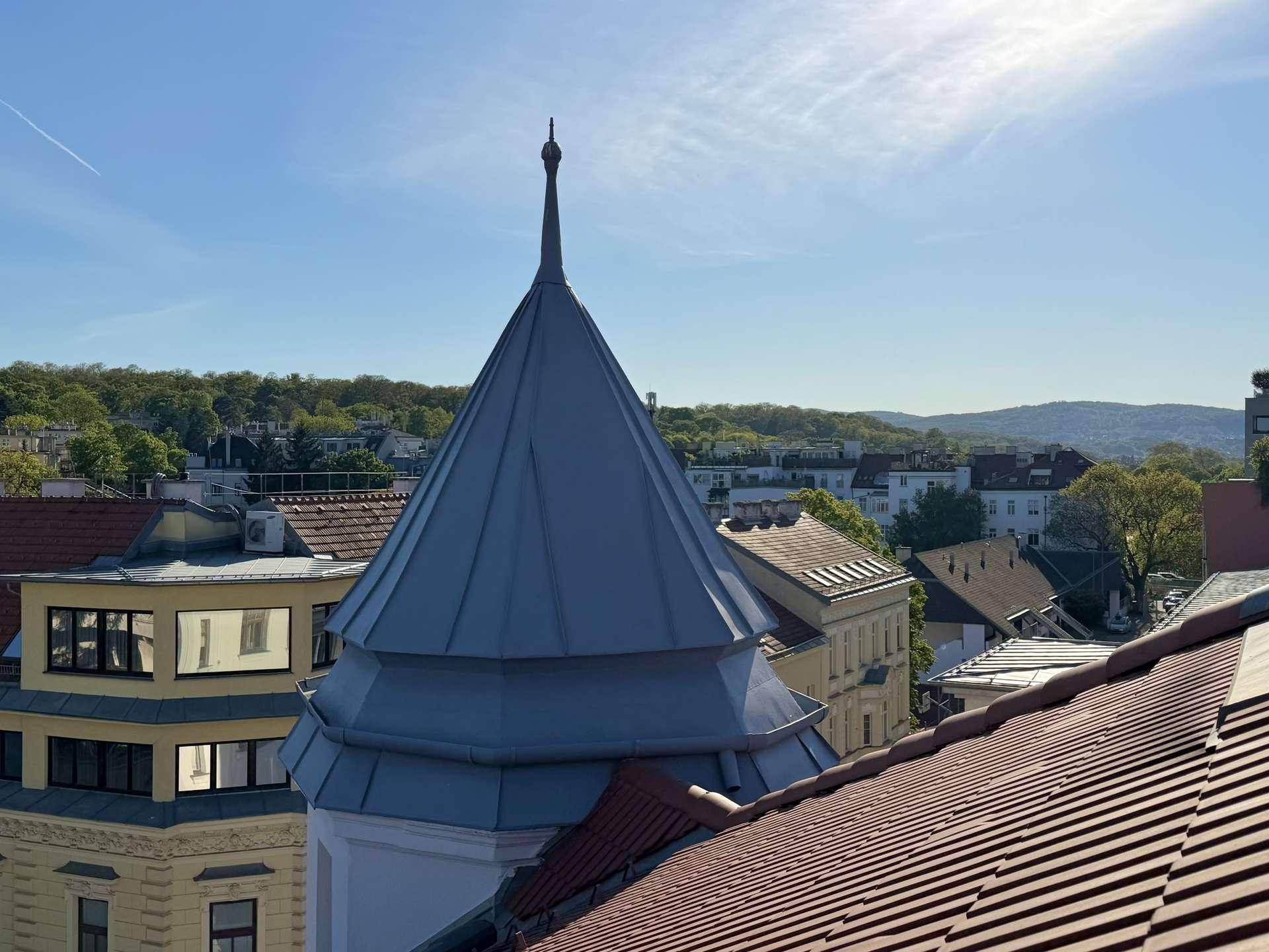 Panoramablick von der Dachterrasse auf historische Gebäude und grüne Hügel in der Ferne.