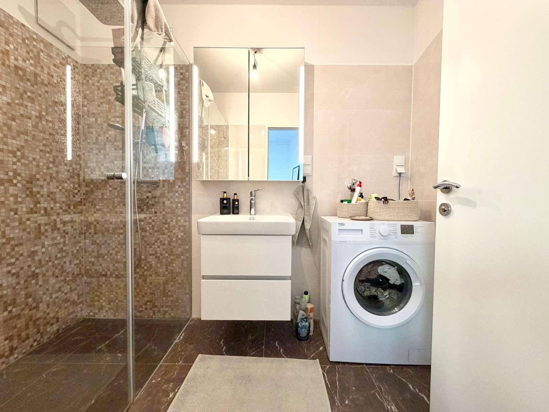 Modernes Badezimmer mit ebenerdiger Dusche, Waschbecken und Waschmaschine.