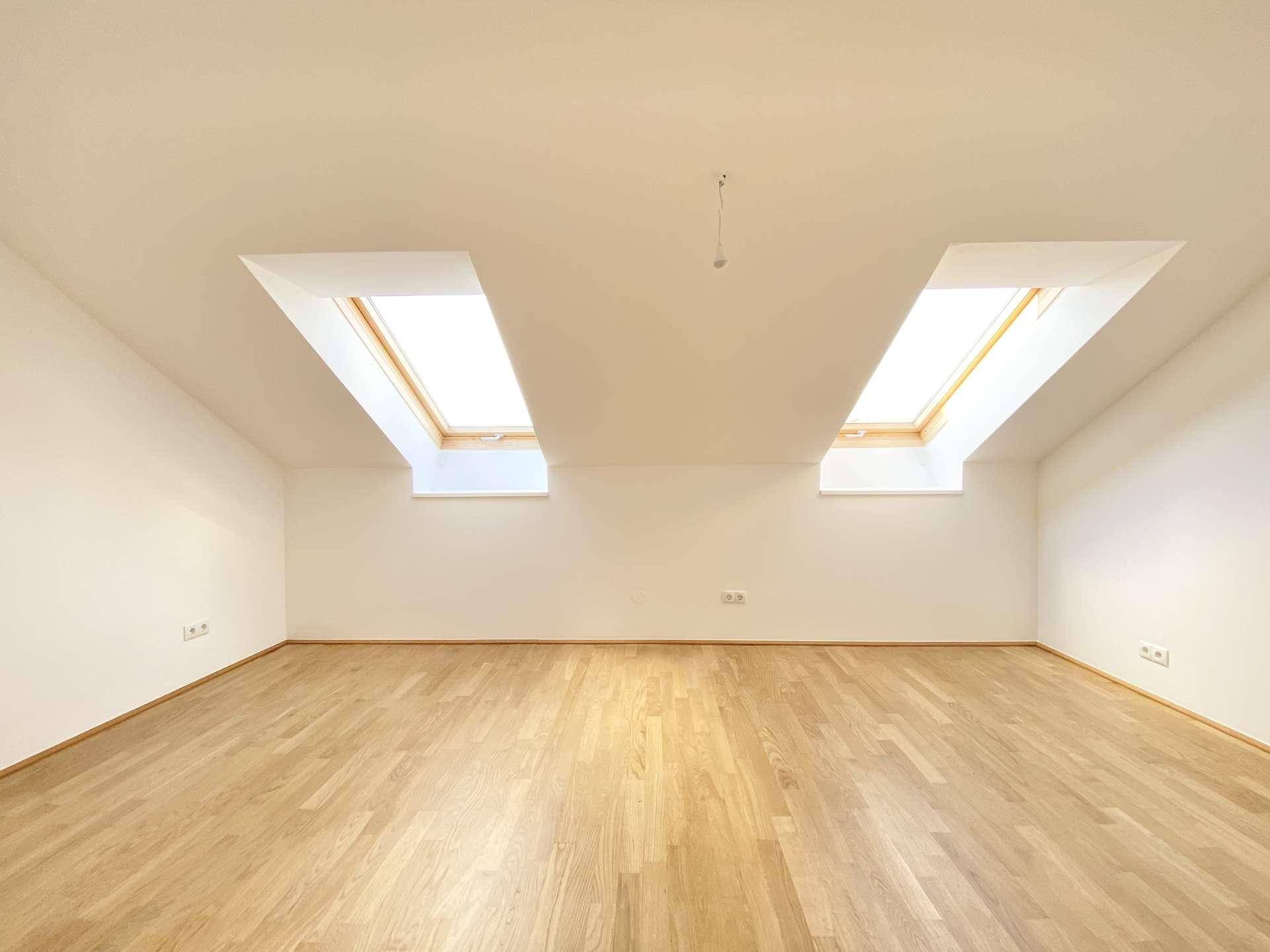 Helles Dachzimmer mit Holzboden und zwei Dachfenstern, ideal für flexible Nutzung.