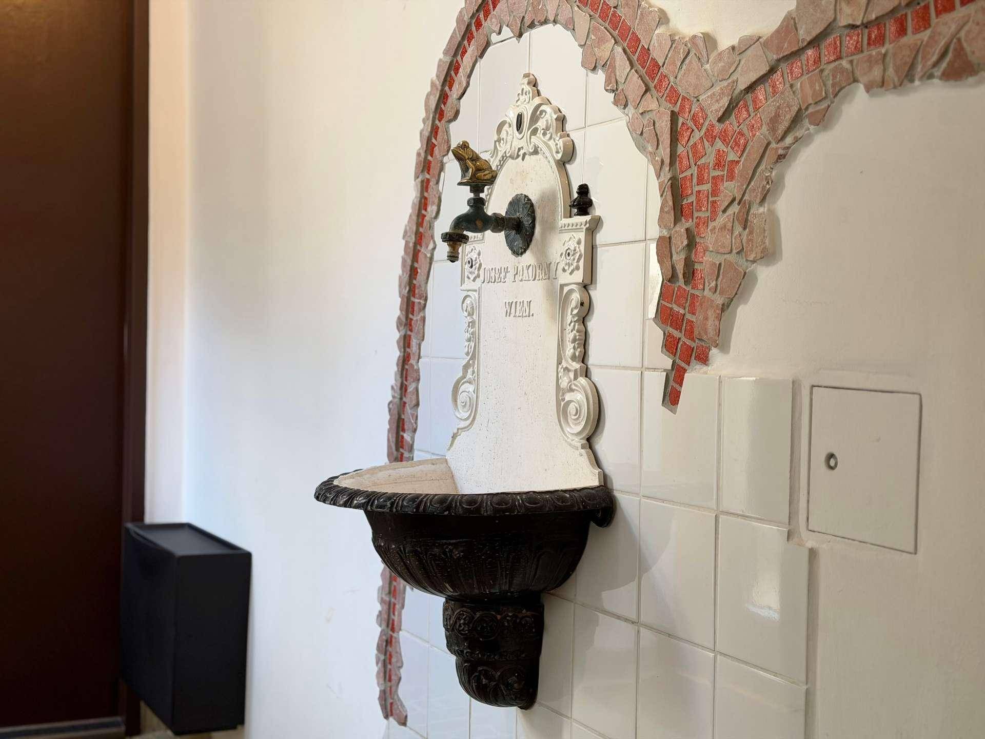 Detailansicht eines historischen Wandbrunnens mit kunstvollen Verzierungen und Fliesenmosaik.