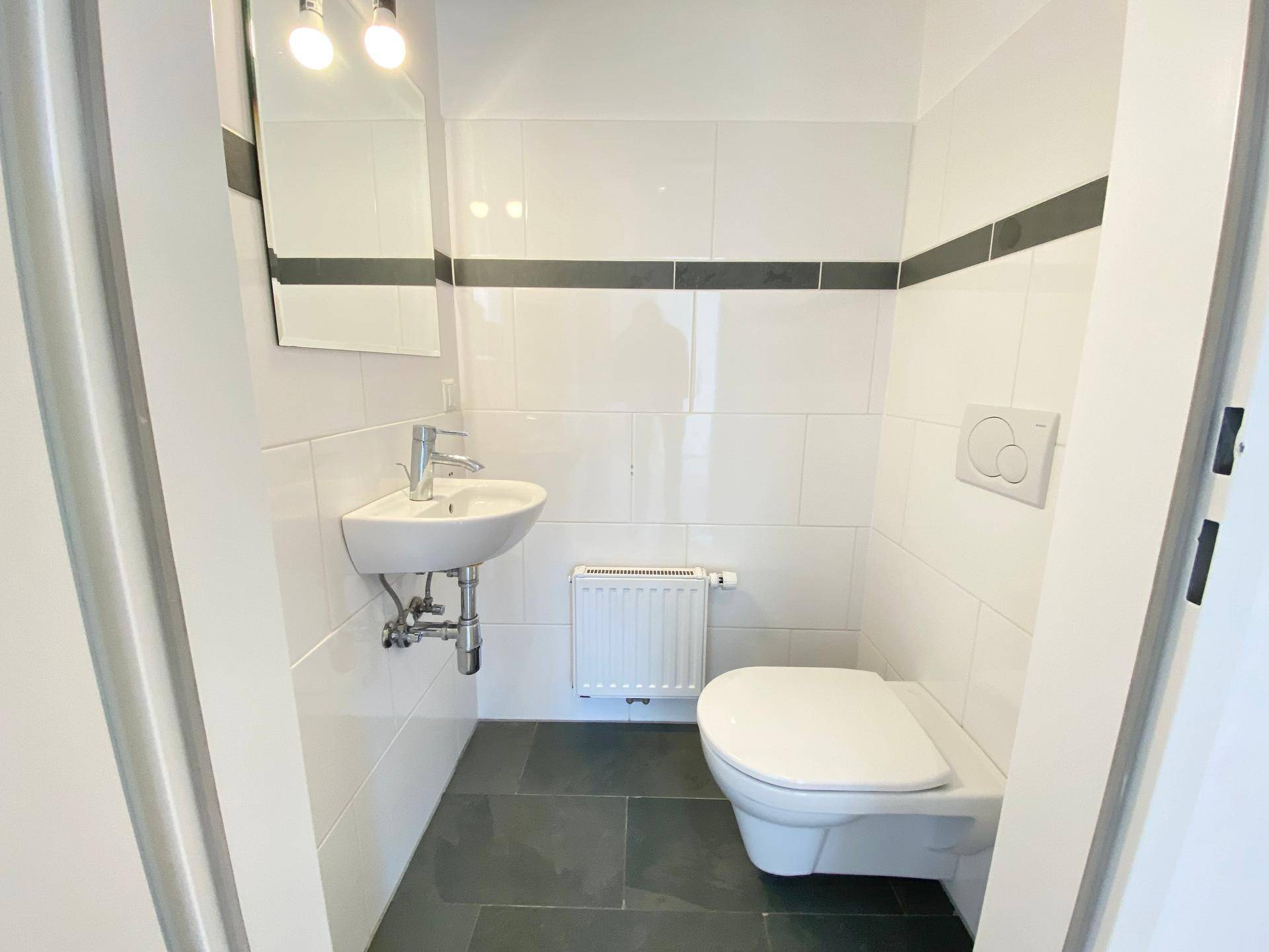 Modernes Gäste-WC mit Wand-WC, kleinem Waschbecken und dunklen Bodenfliesen.