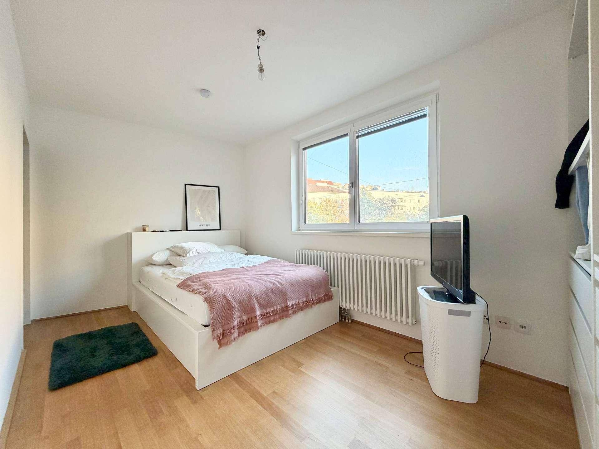 Helles Schlafzimmer mit Doppelbett, Holzfußboden und Fenster mit Stadtblick.